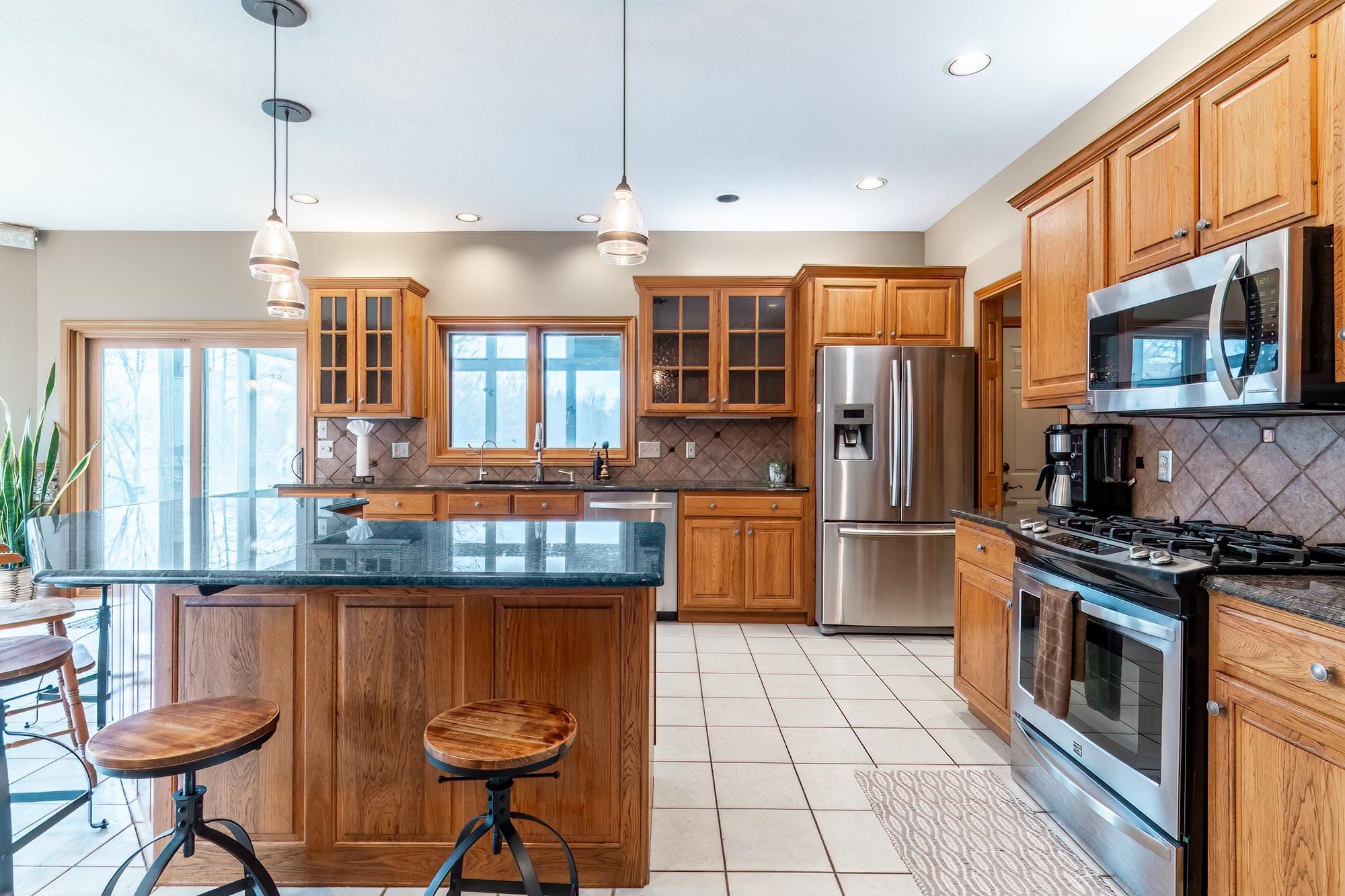 Kitchen with stainless steel appliances, wood finish cabinets, light tile patterned floors, glass insert cabinets, and a kitchen bar