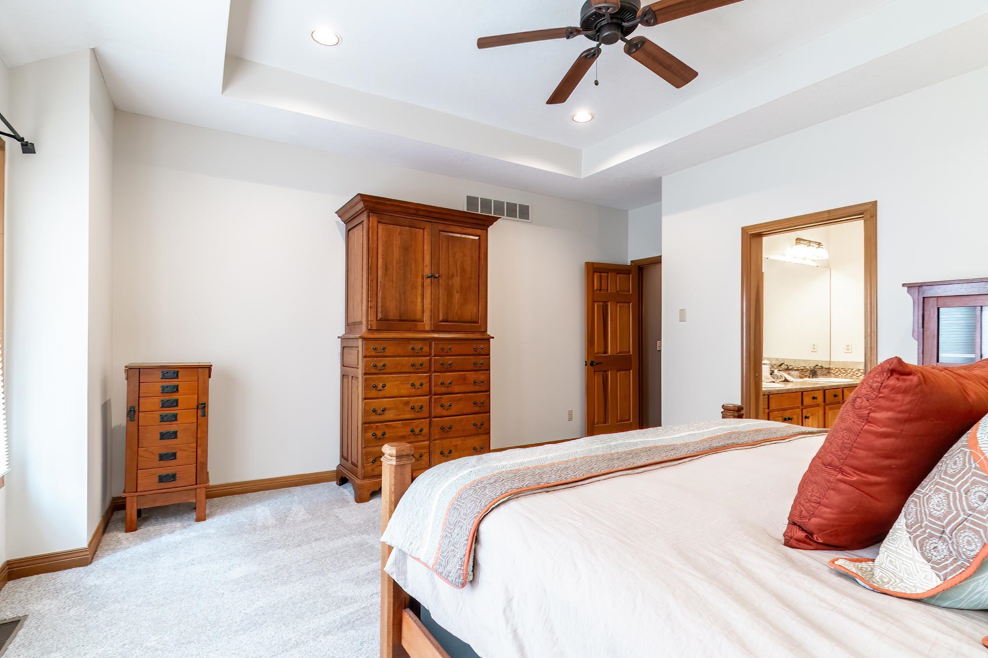 Bedroom featuring a raised ceiling, recessed lighting, light colored carpet, a ceiling fan, and ensuite bath