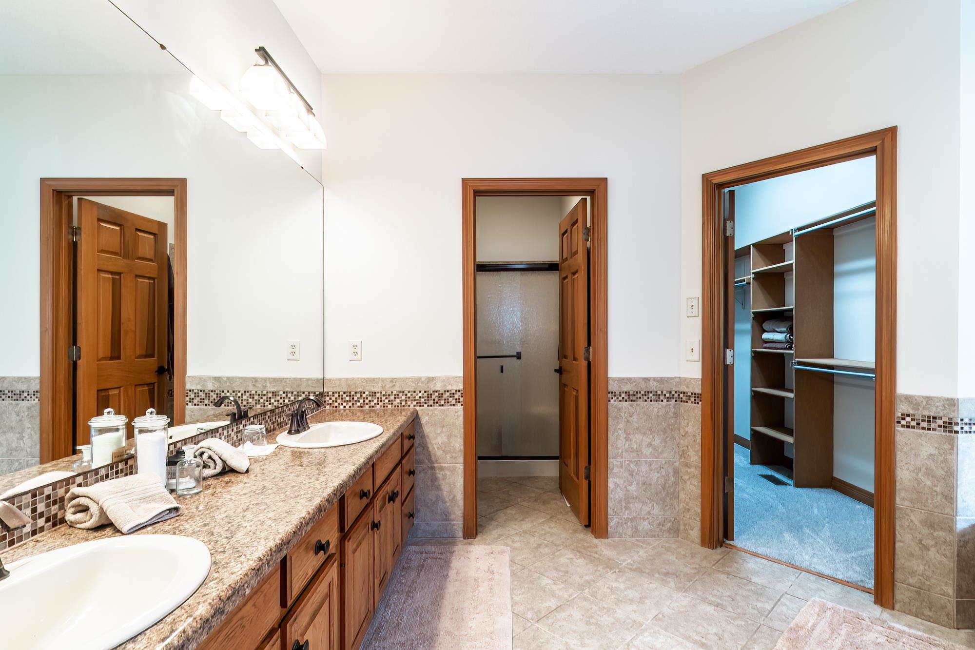 Bathroom featuring wainscoting, double vanity, a walk in closet, tile walls, and light tile patterned floors