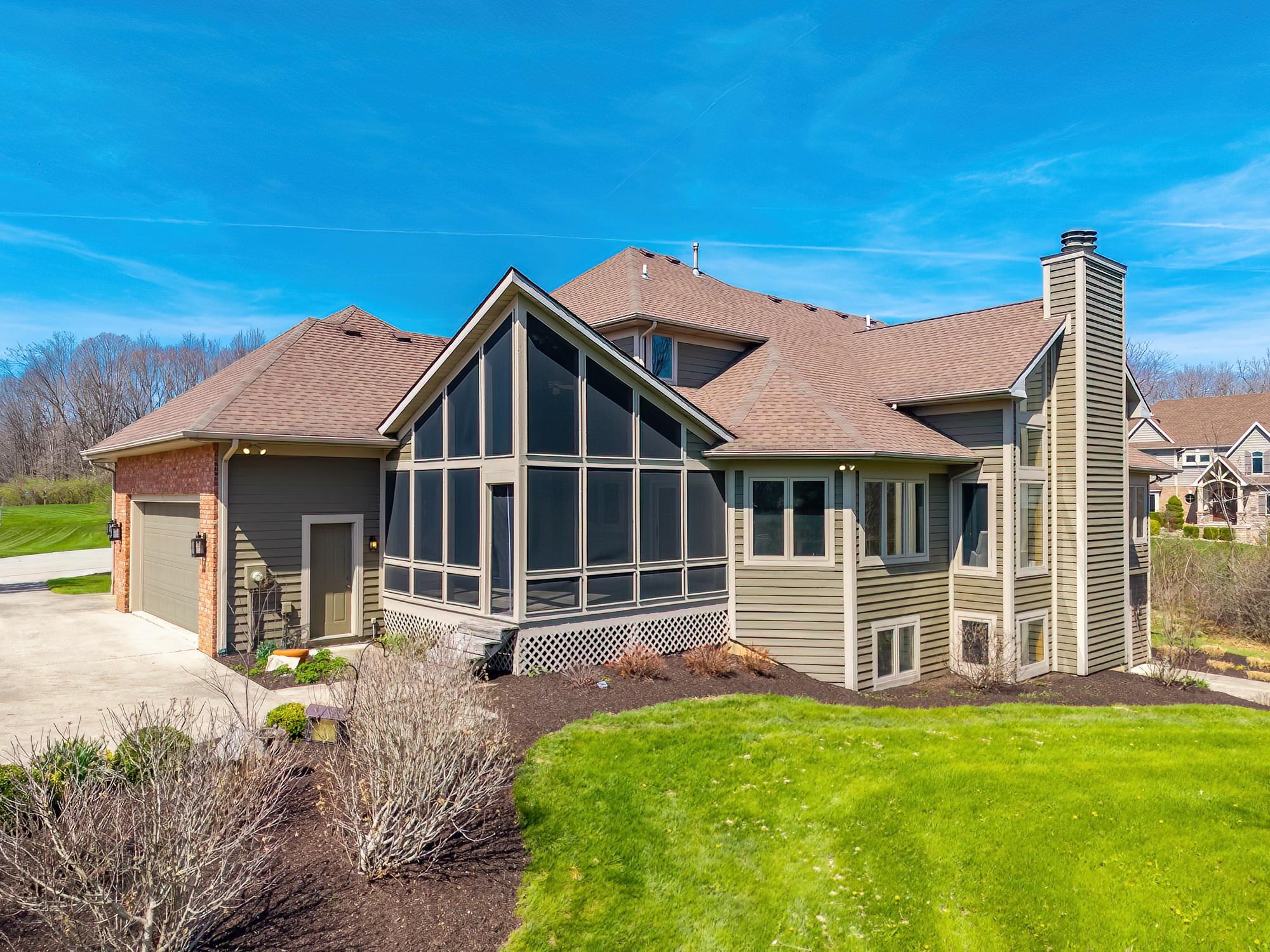 Rear view of property with a sunroom, a garage, a chimney, a lawn, and a shingled roof