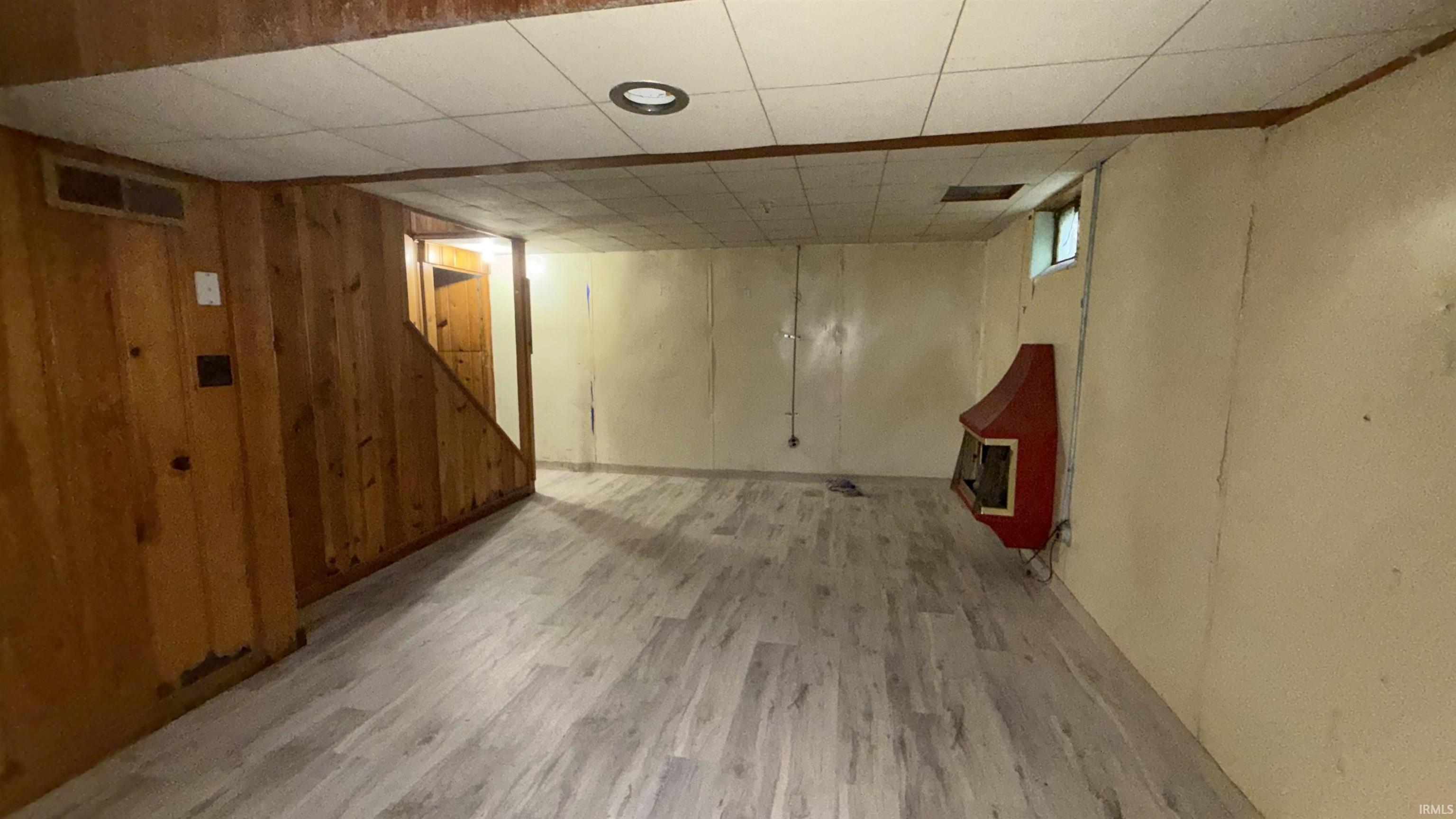 Below grade area featuring light wood-style flooring, wooden walls, and a drop ceiling