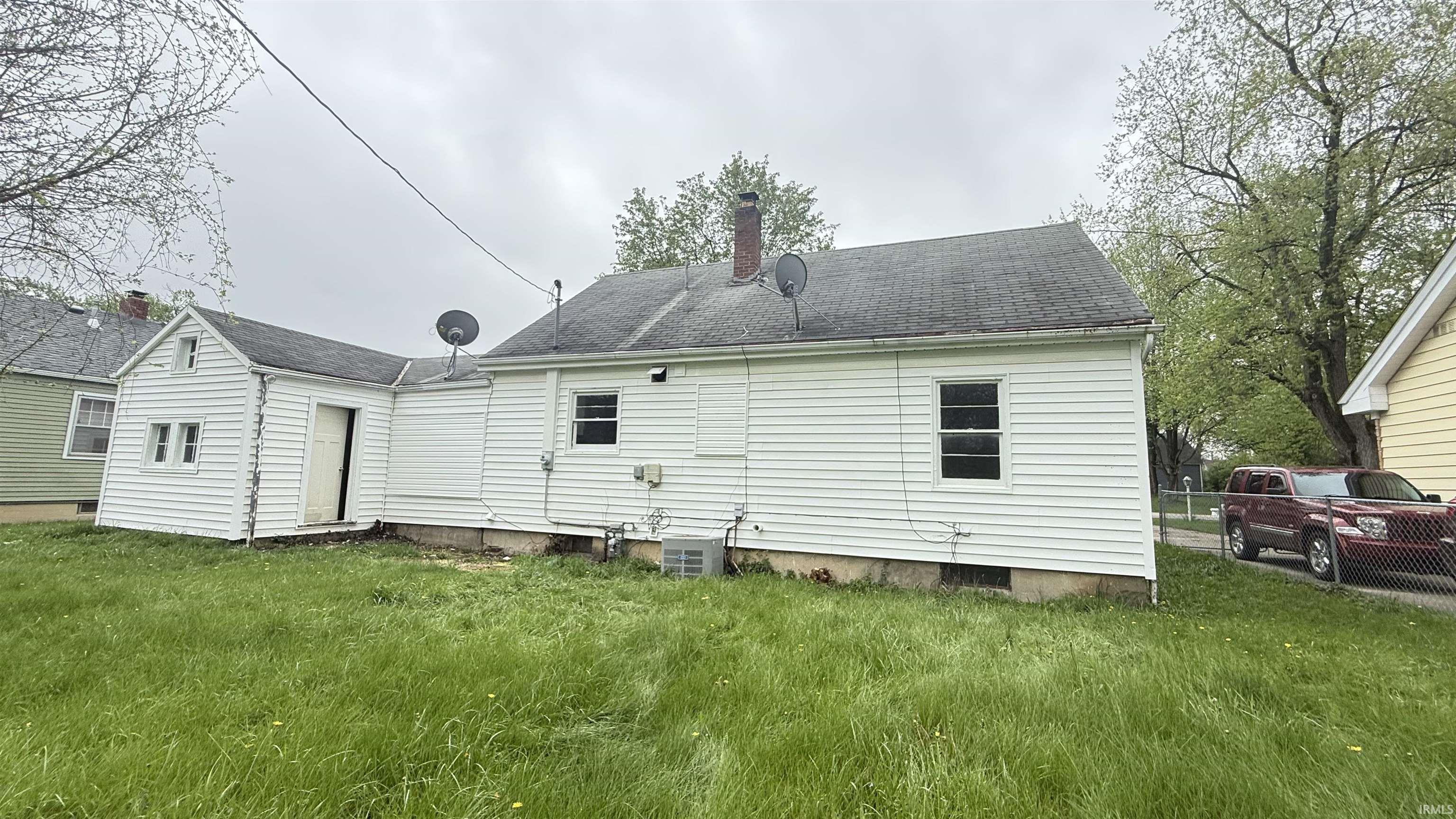 Rear view of house featuring a chimney, a yard, and roof with shingles