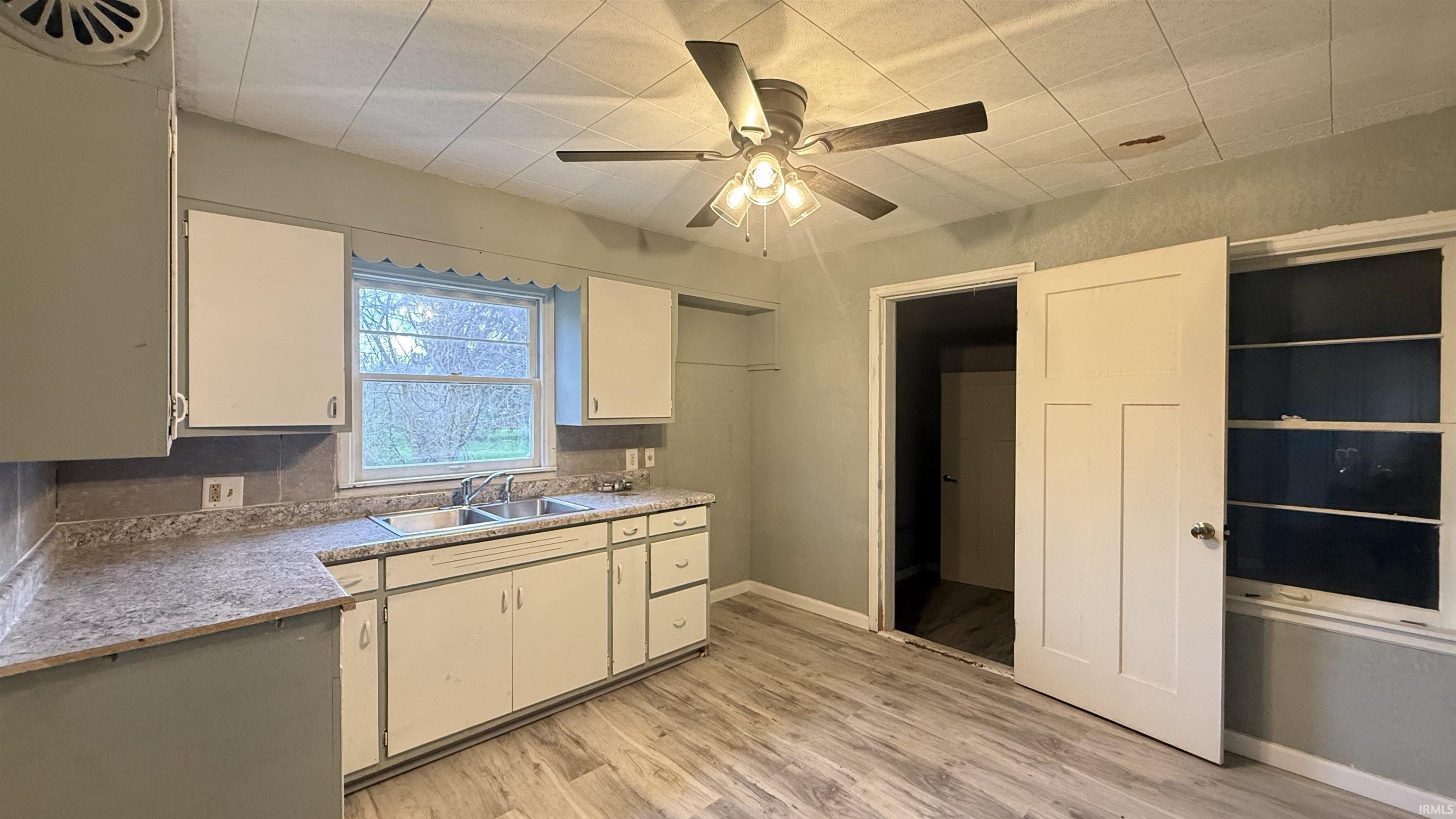 Kitchen with light wood-style floors, ceiling fan, light countertops, and white cabinetry