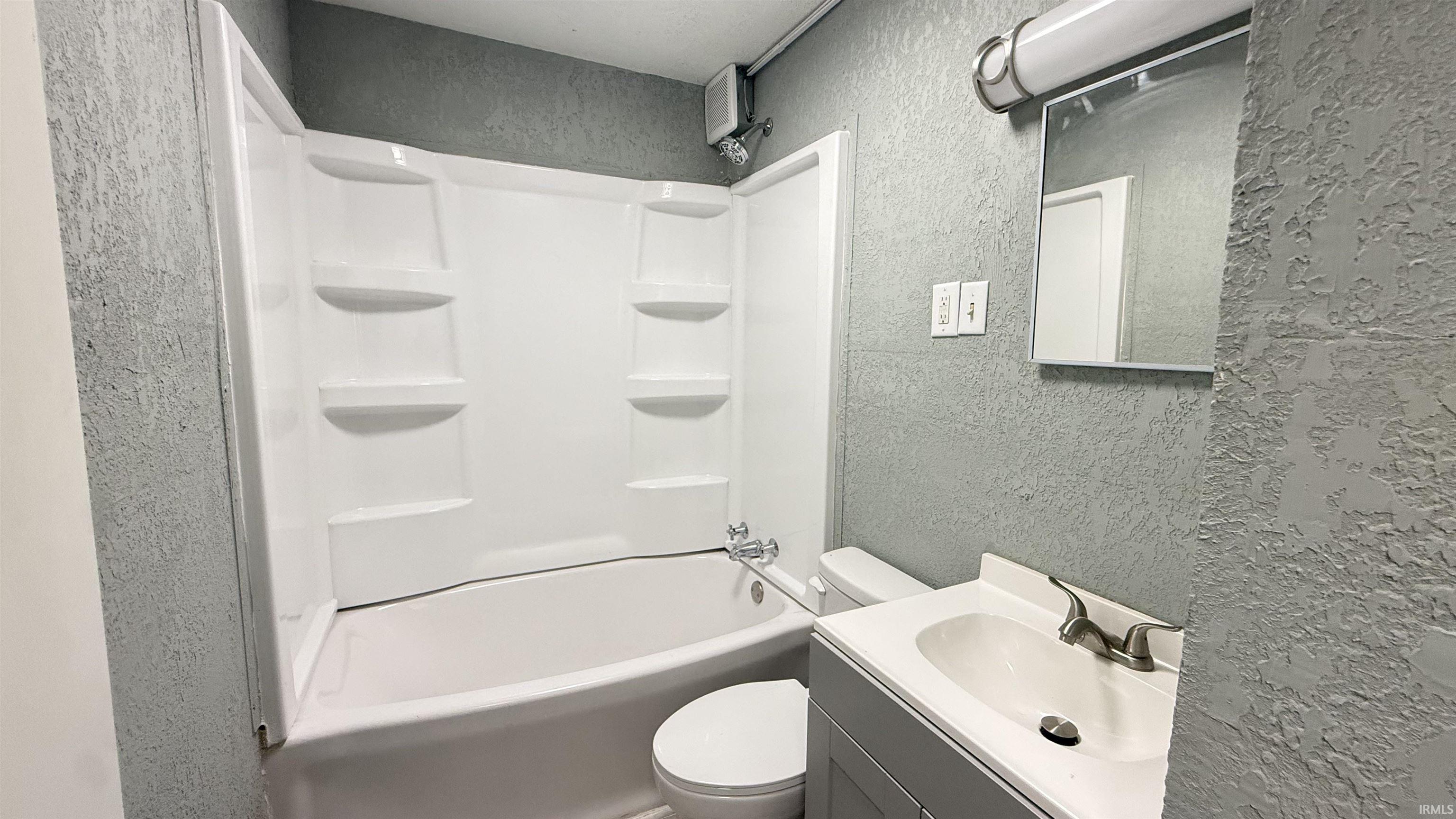 Full bathroom with a textured wall, vanity, and bathing tub / shower combination