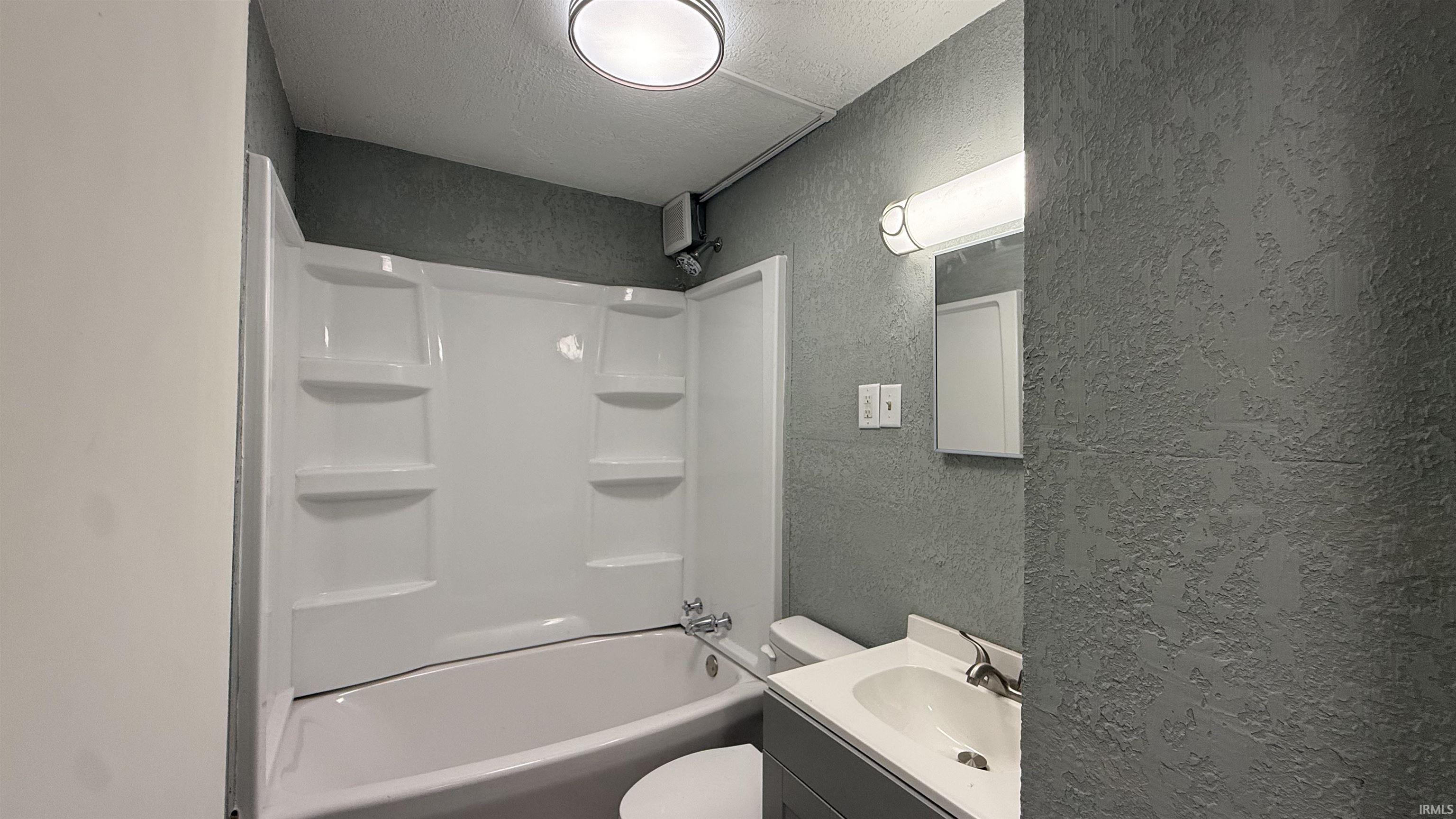 Bathroom with a textured wall, vanity, a textured ceiling, and shower / bath combination