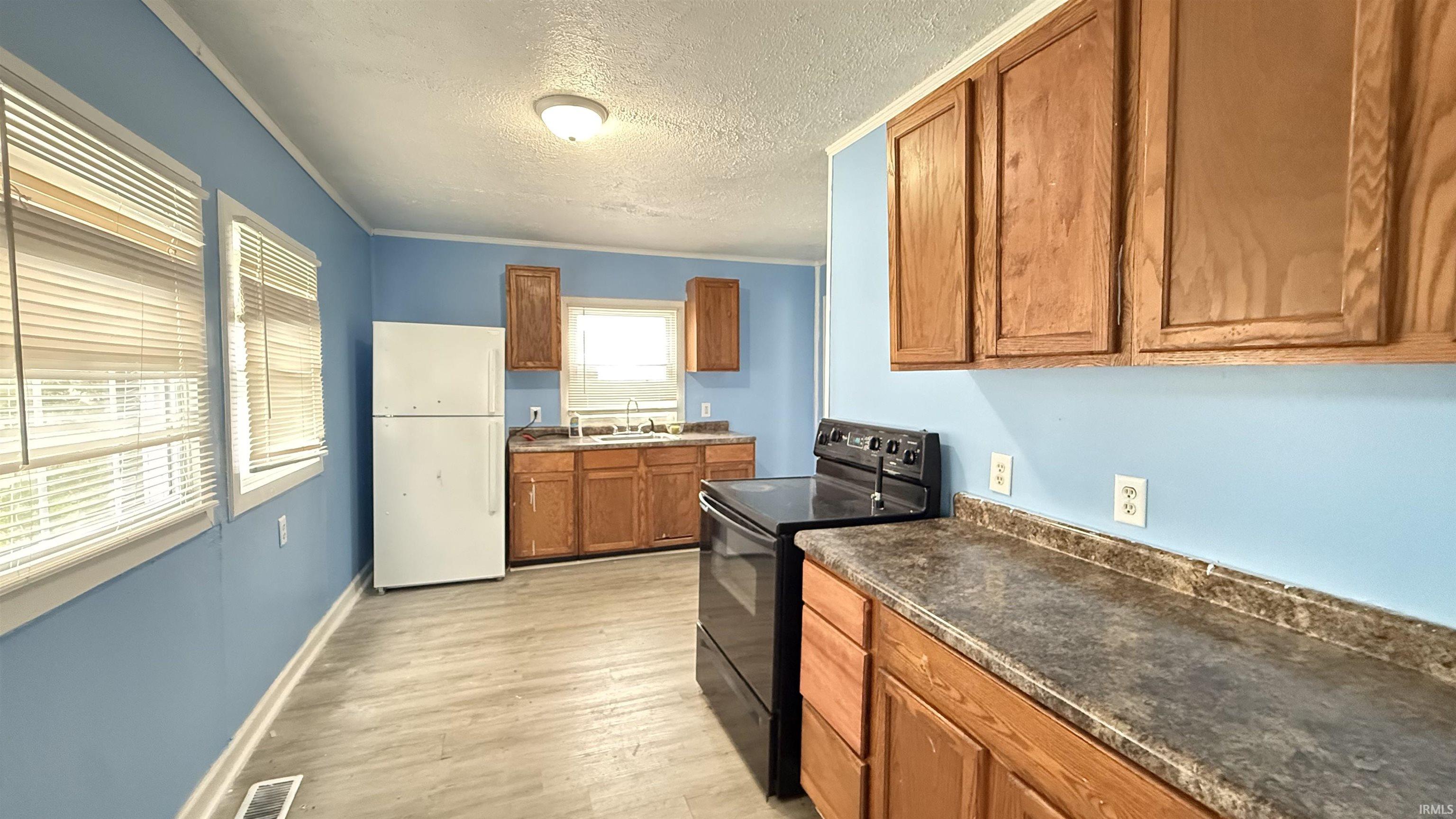Kitchen with wood finish cabinets, electric range, freestanding refrigerator, dark countertops, and a textured ceiling