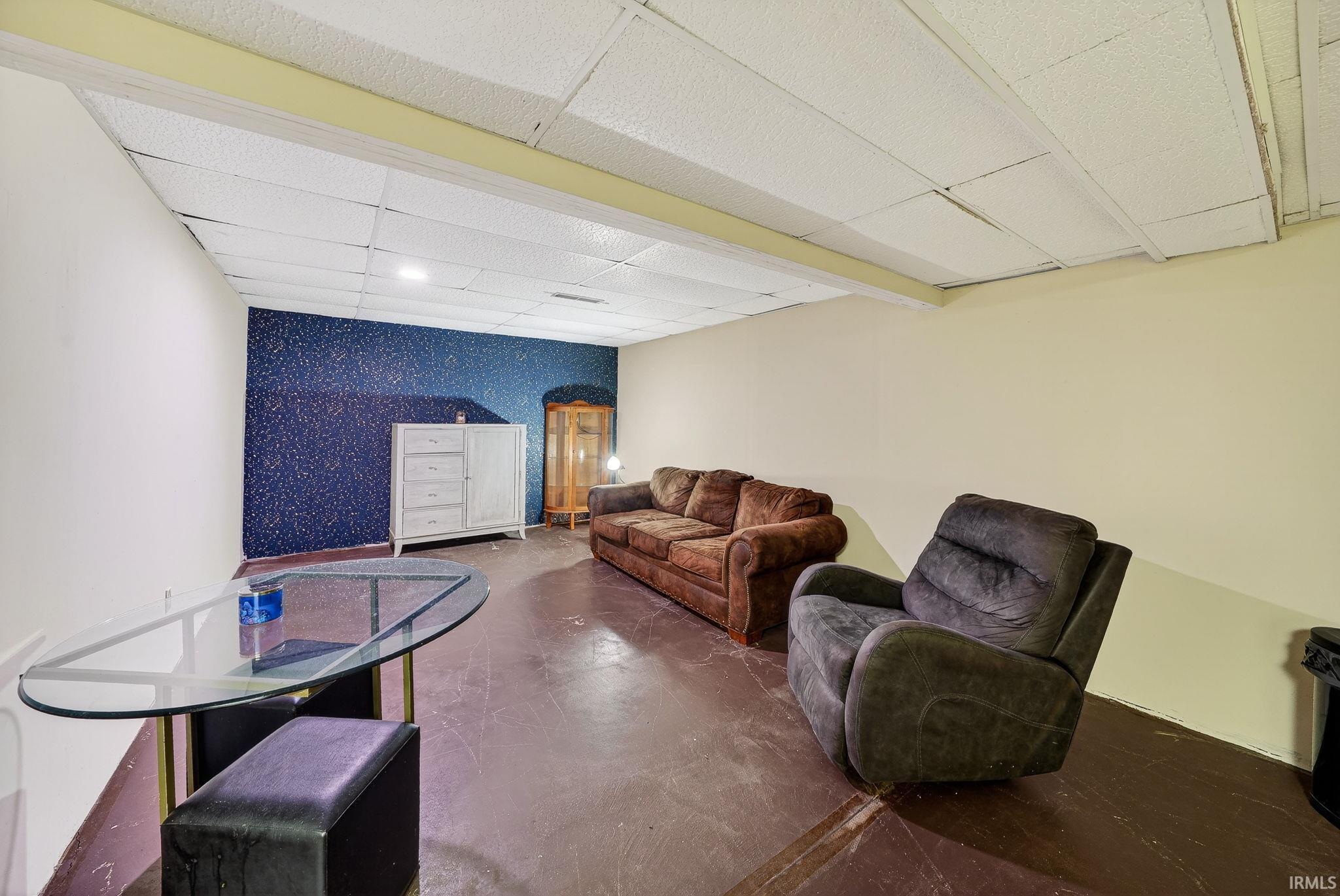 Living area with an accent wall, a drop ceiling, finished concrete flooring, and wallpapered walls