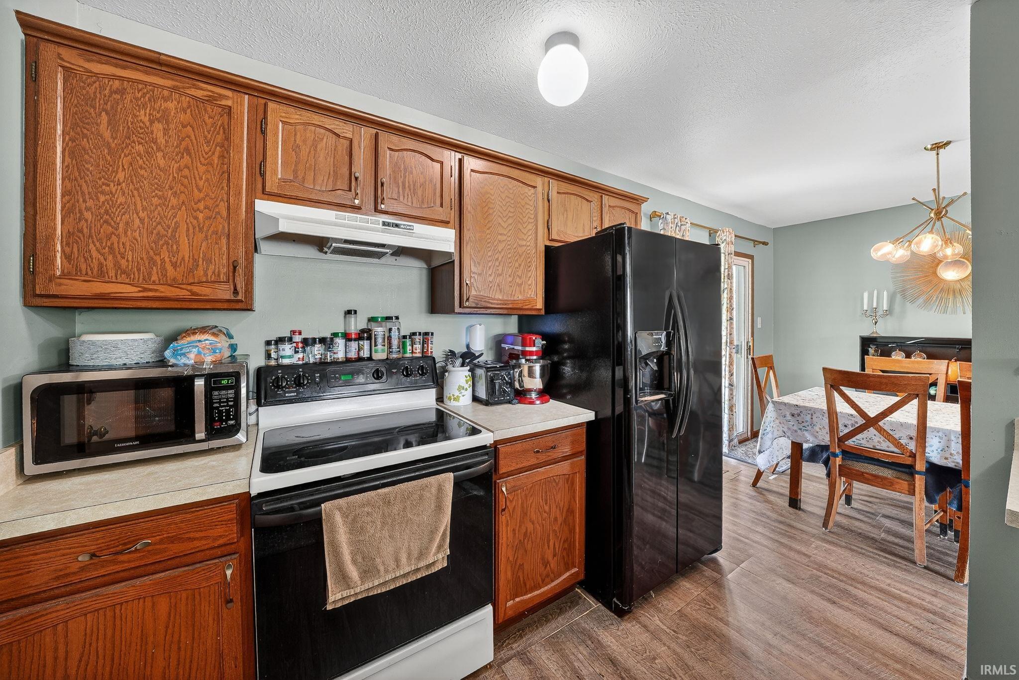 Kitchen featuring black appliances, light countertops, hanging lights, dark wood-type flooring, and wood finish cabinets