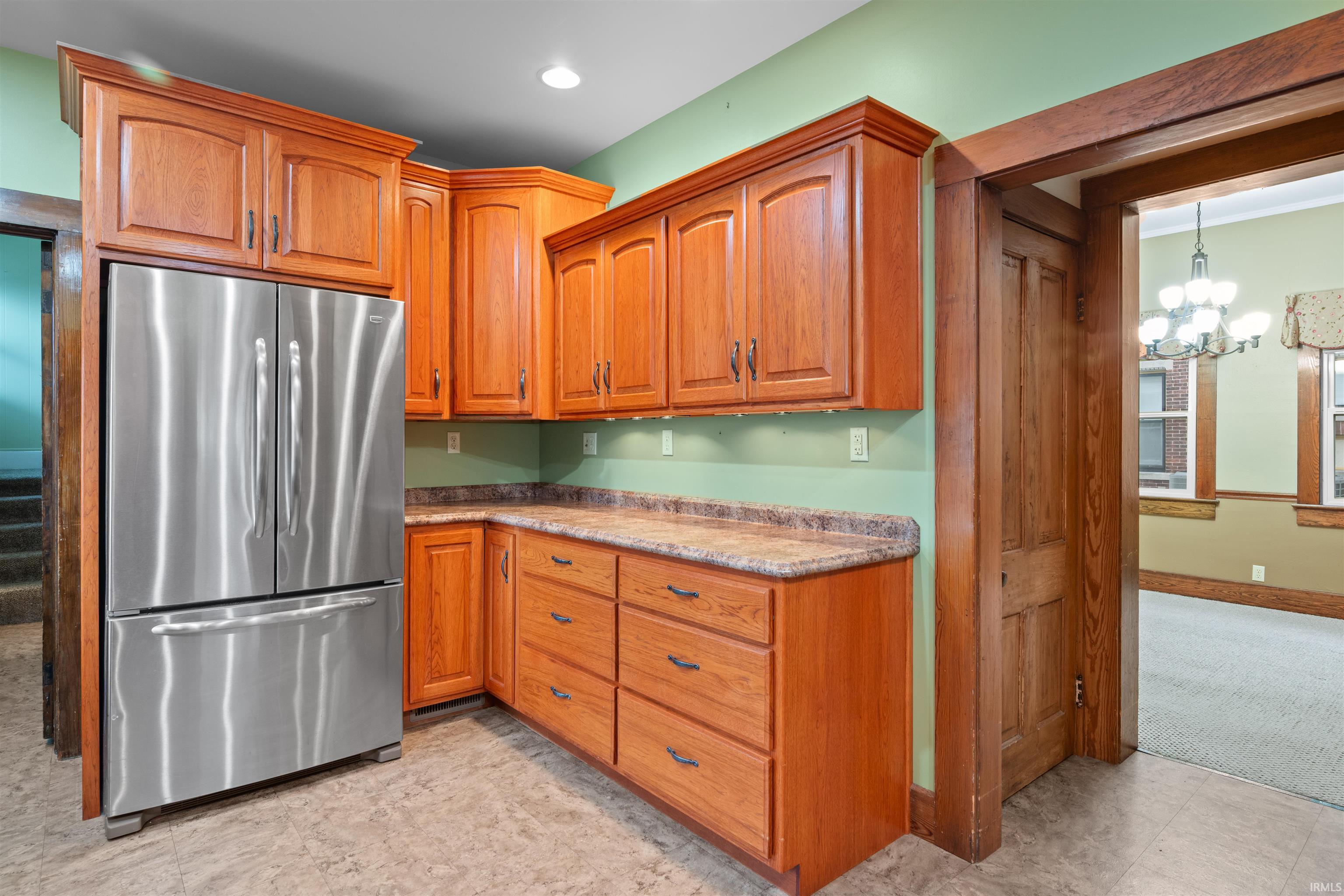 Kitchen with freestanding refrigerator, suspended lighting, wood finish cabinets, and light countertops