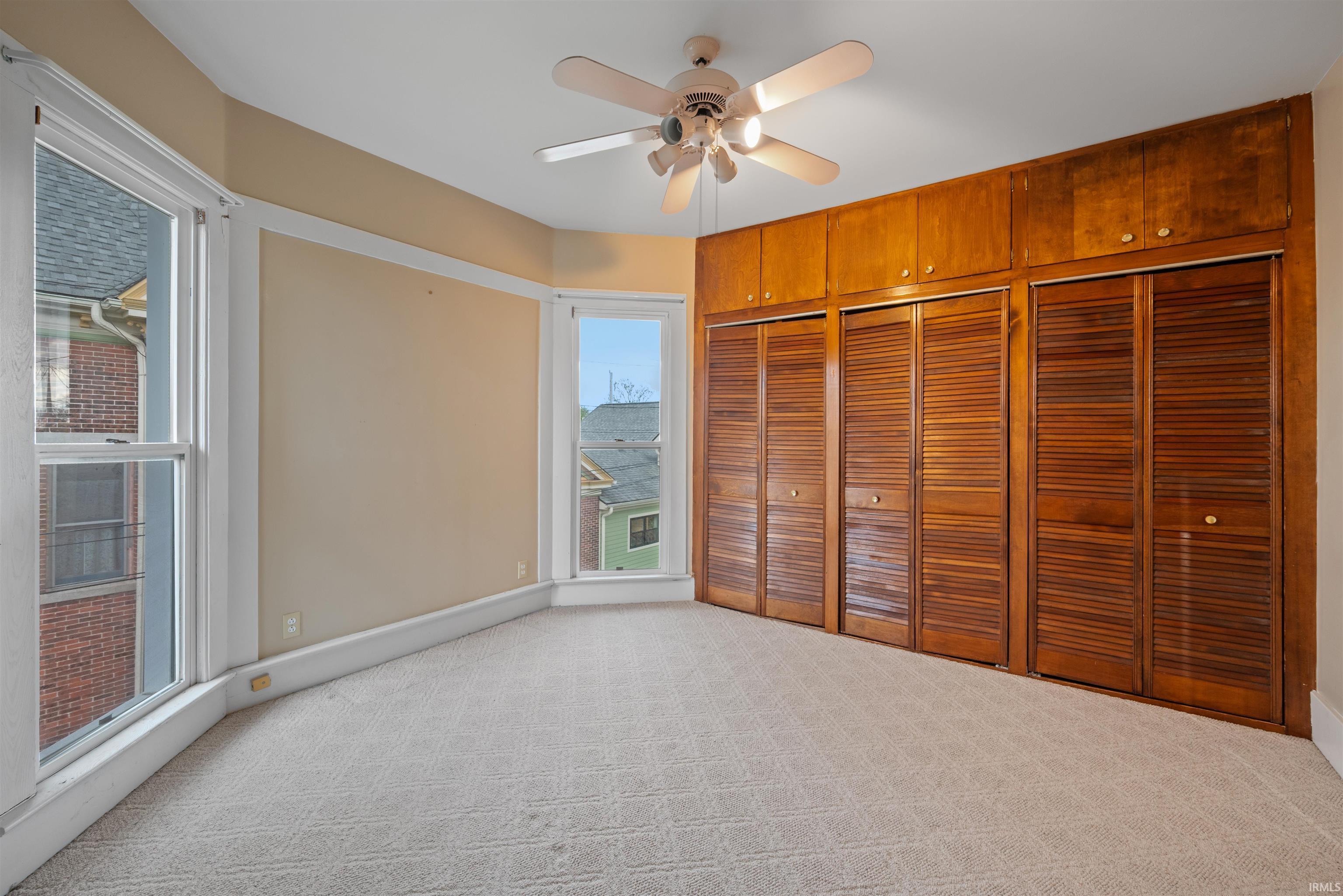 Unfurnished bedroom featuring light carpet, two closets, and ceiling fan