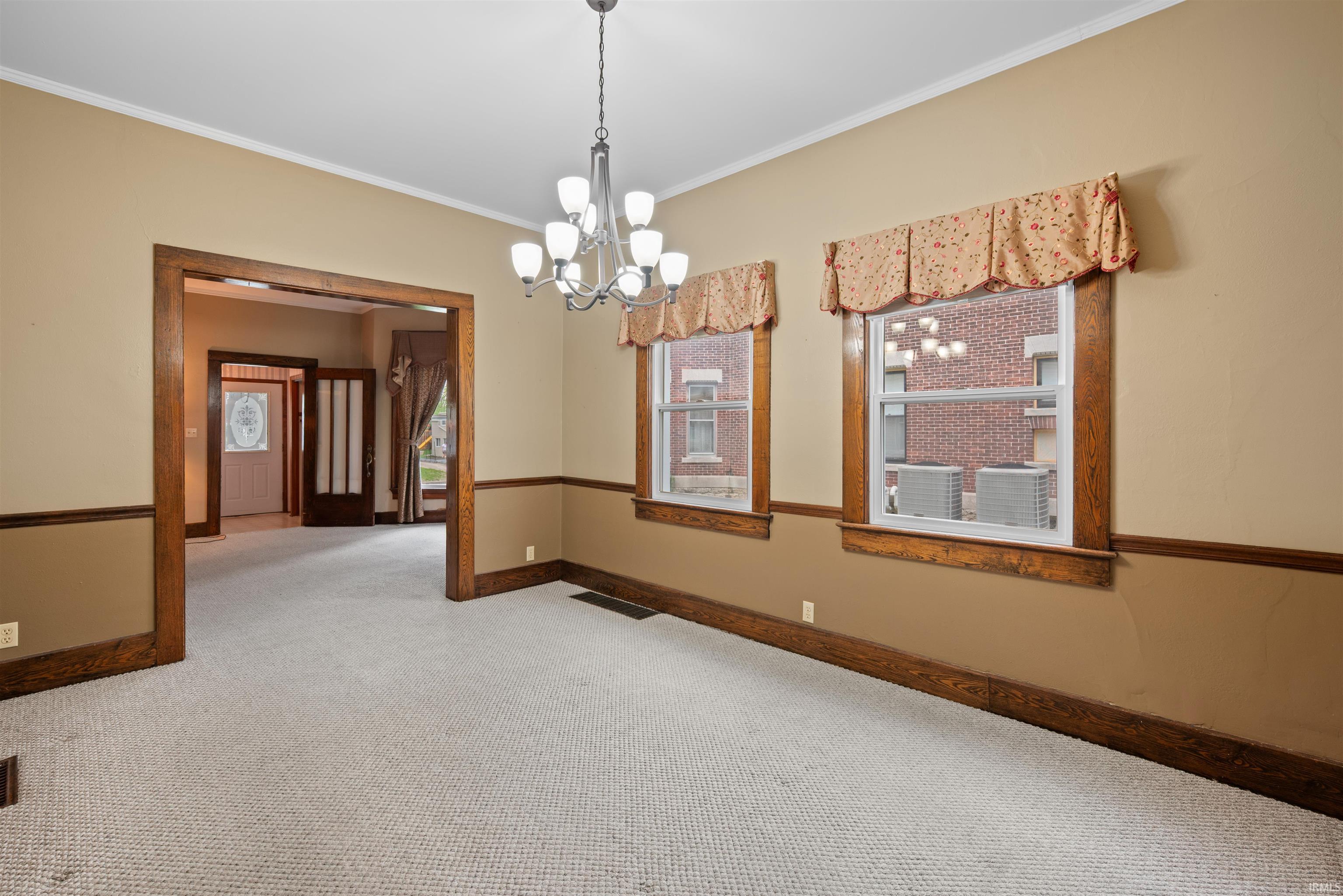Spare room with light colored carpet, a chandelier, crown molding, and plenty of natural light