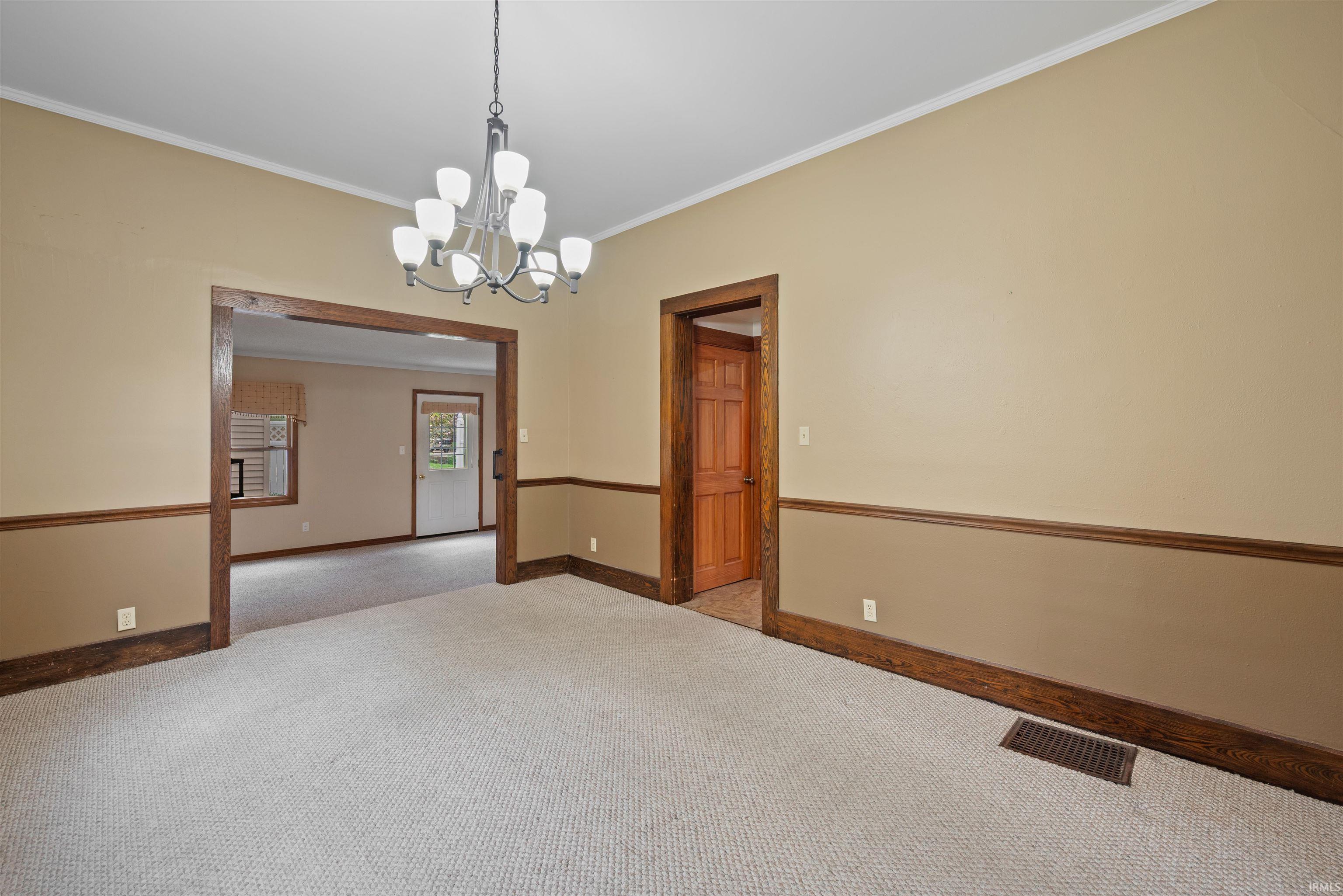 Empty room featuring light carpet, crown molding, and suspended lighting