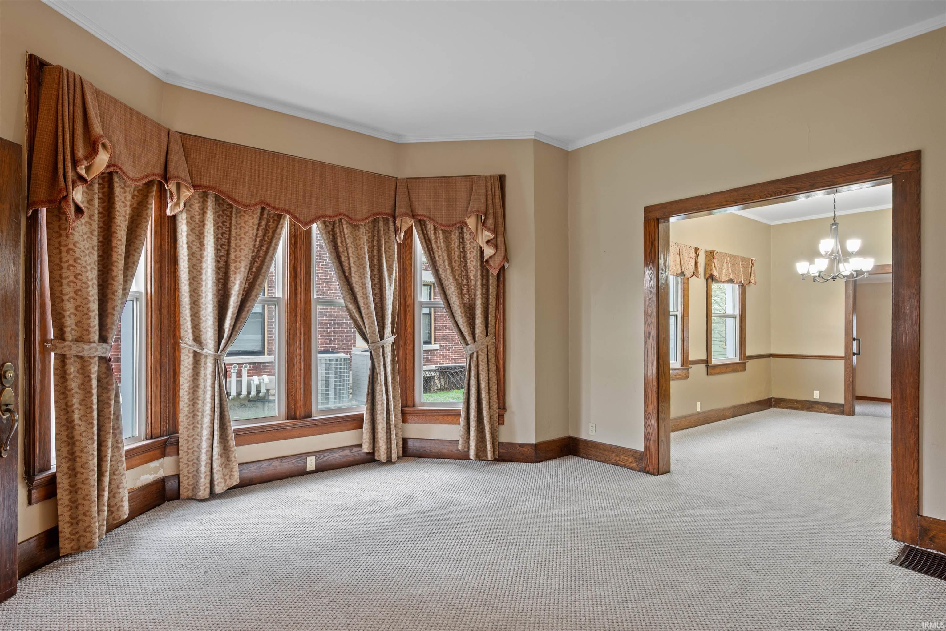 Empty room featuring light colored carpet, ornamental molding, and hanging lights
