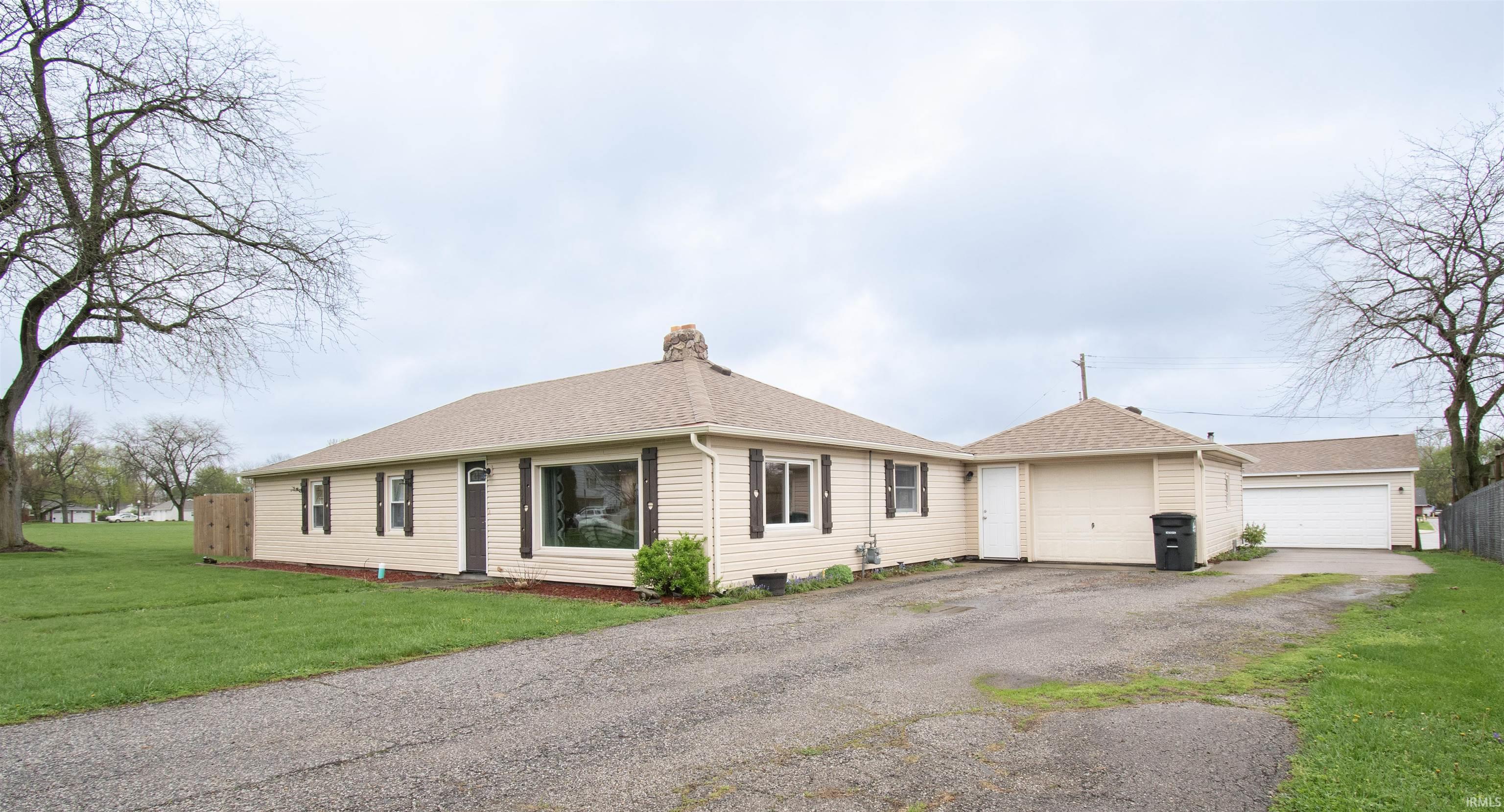Ranch-style home featuring a chimney, a garage, a shingled roof, and a front lawn