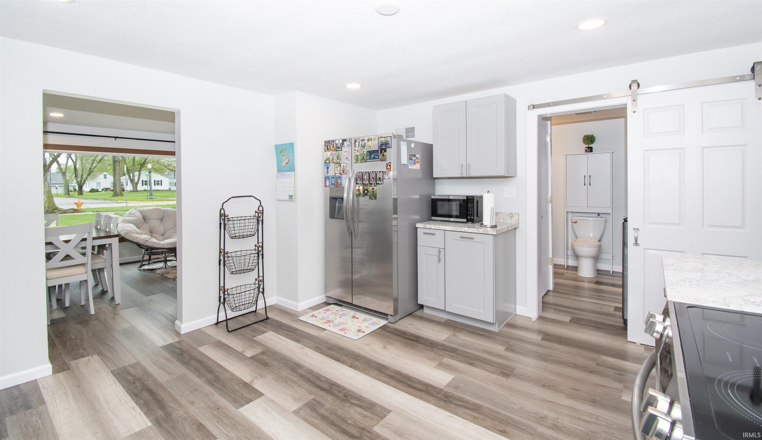 Kitchen featuring a barn door, stainless steel appliances, light wood-type flooring, recessed lighting, and light stone counters