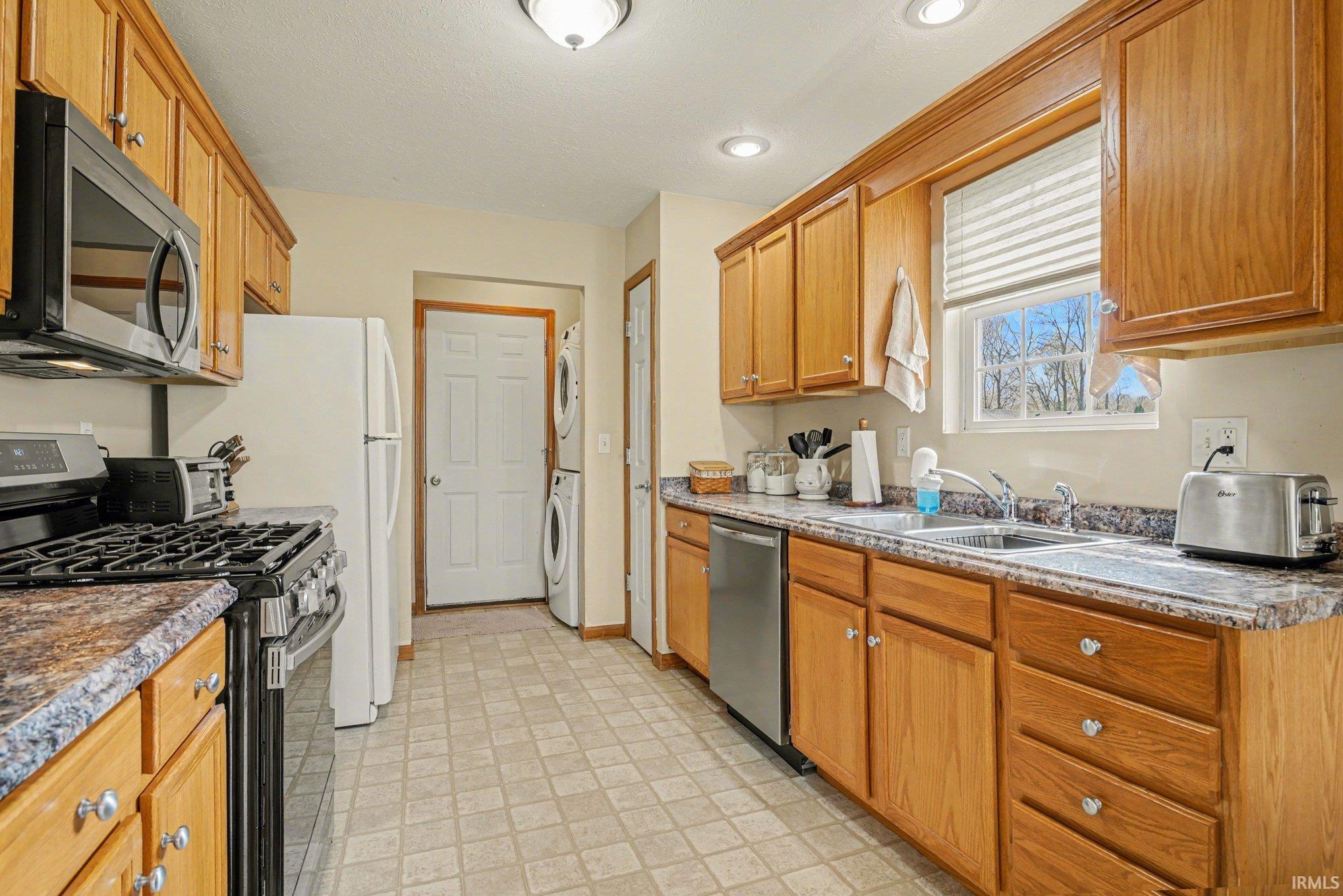 Kitchen with stainless steel appliances, stacked washer and dryer, wood finish cabinetry, and light flooring