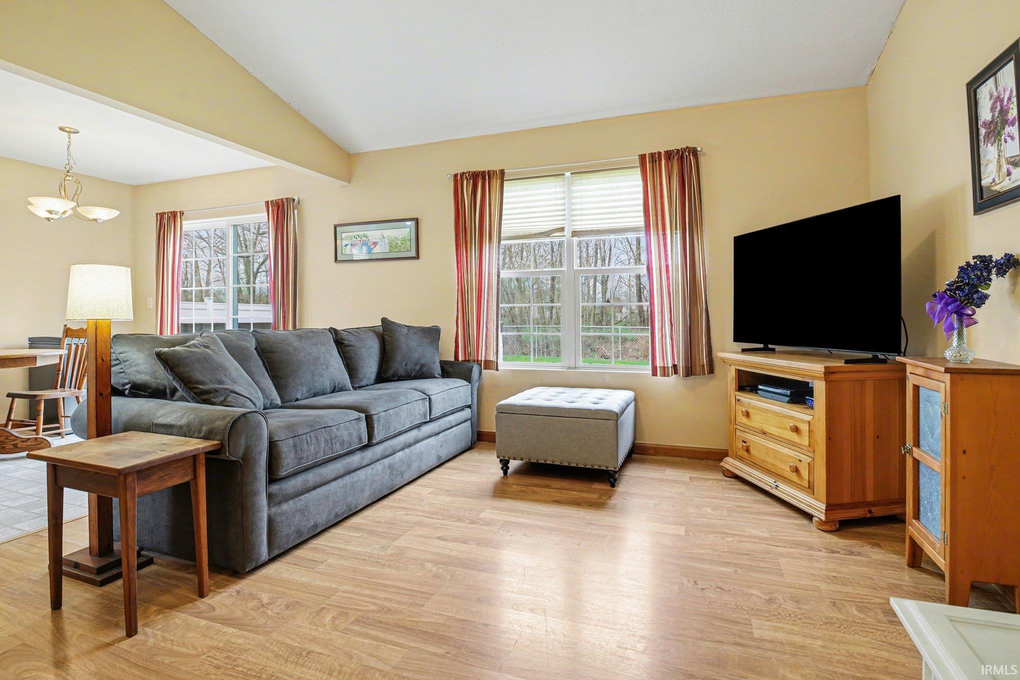 Living room with vaulted ceiling, light wood finished floors, plenty of natural light, and suspended lighting