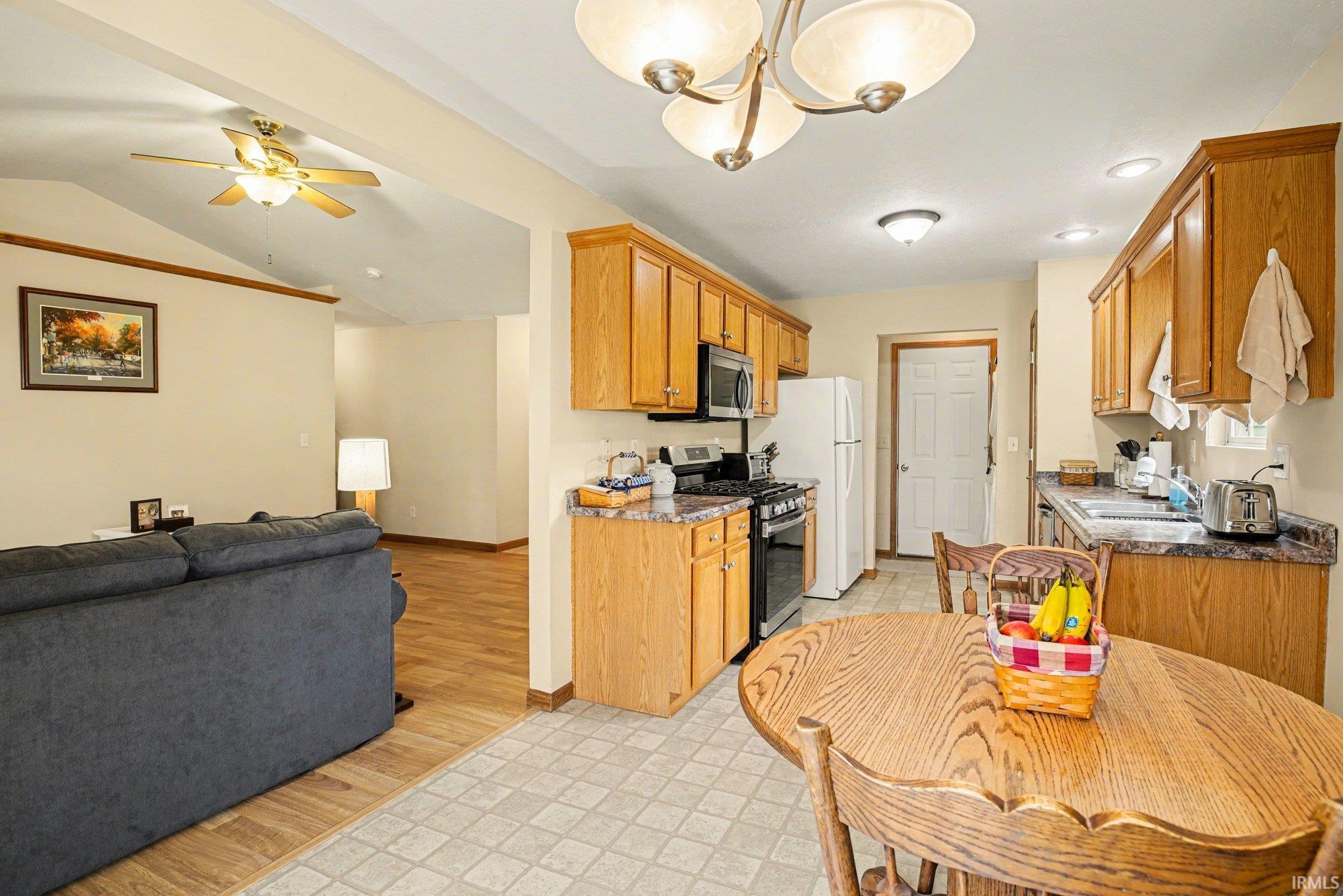 Kitchen with stainless steel appliances, open floor plan, ceiling fan, suspended lighting, and wood finish cabinetry
