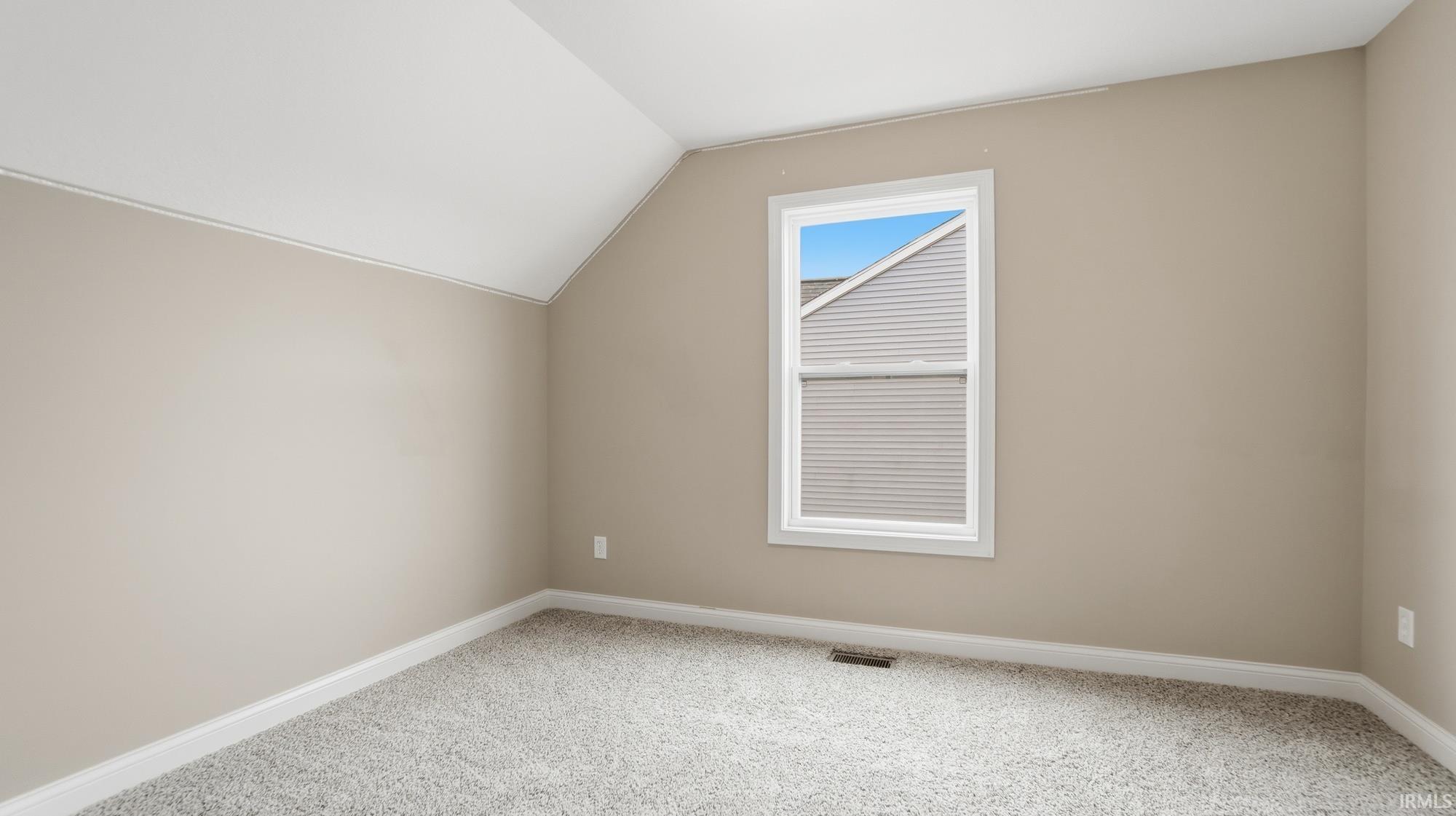Bonus room with vaulted ceiling and light colored carpet