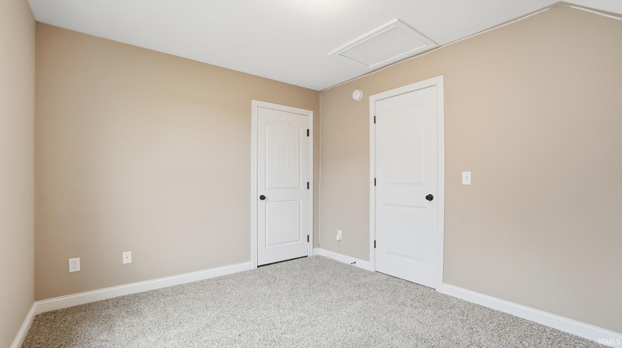 Carpeted empty room featuring attic access and baseboards