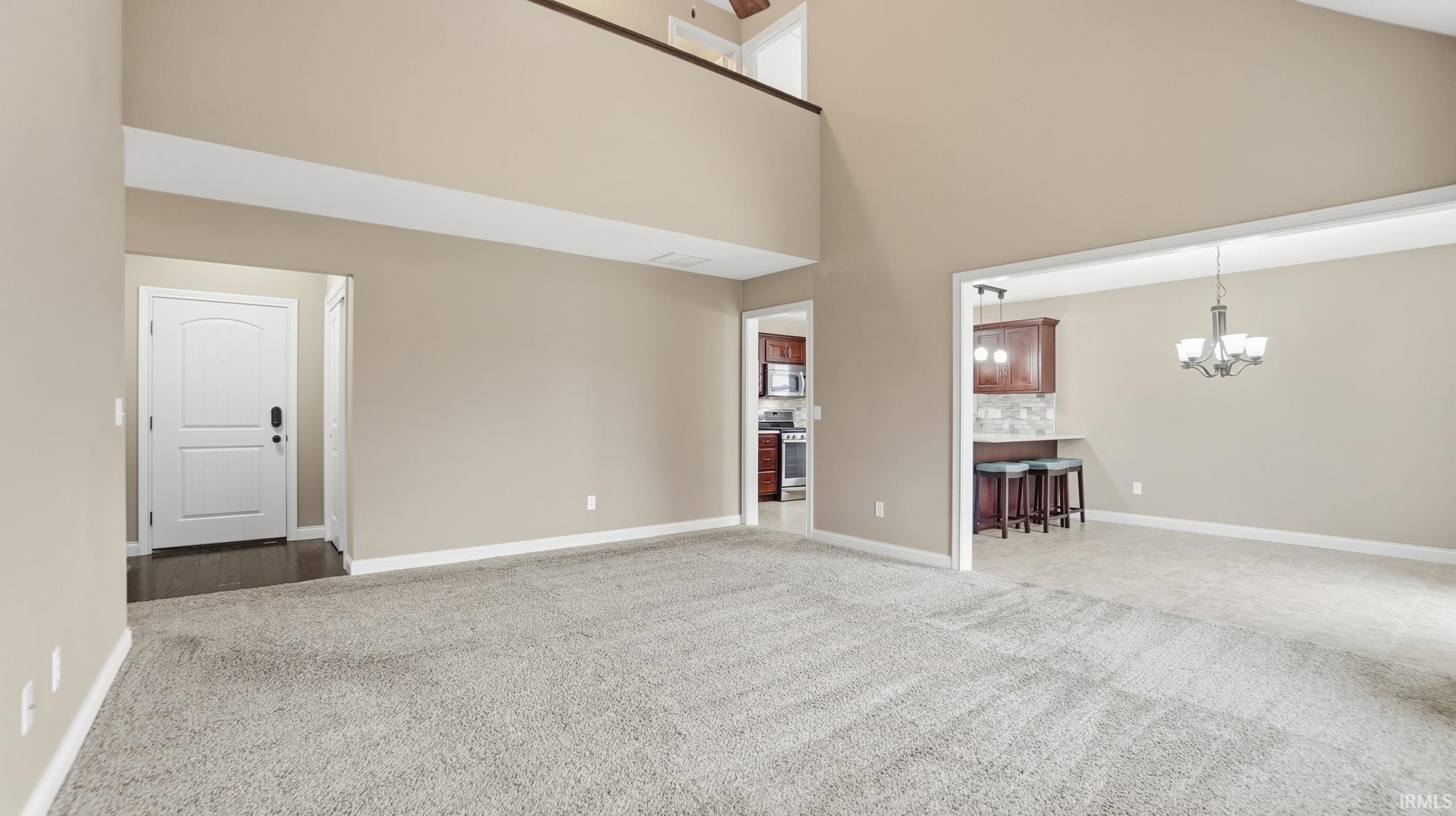 Unfurnished living room with light carpet, a high ceiling, and hanging lights