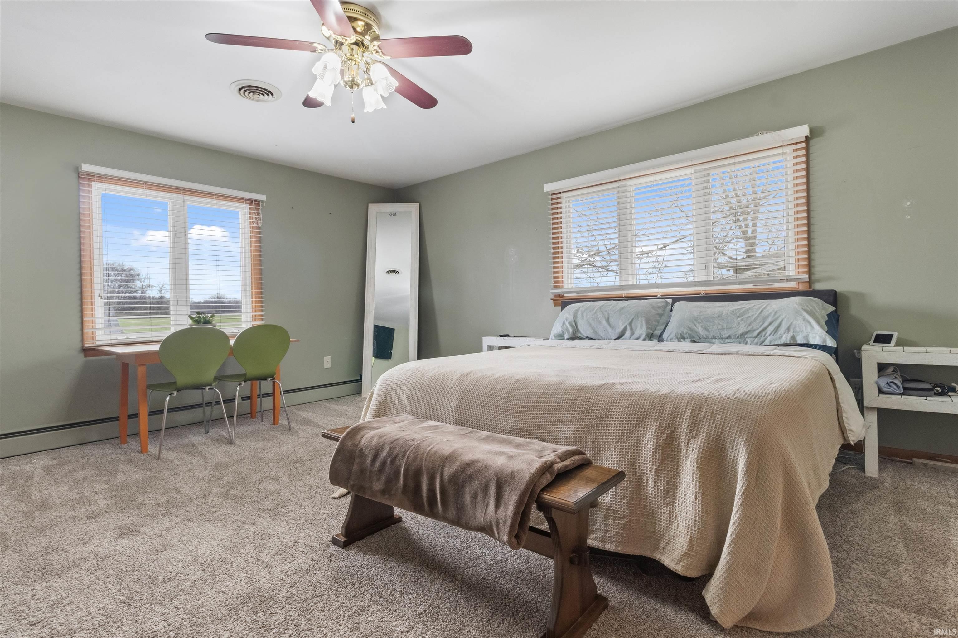 Bedroom featuring light colored carpet, multiple windows, a ceiling fan, and a baseboard heating unit