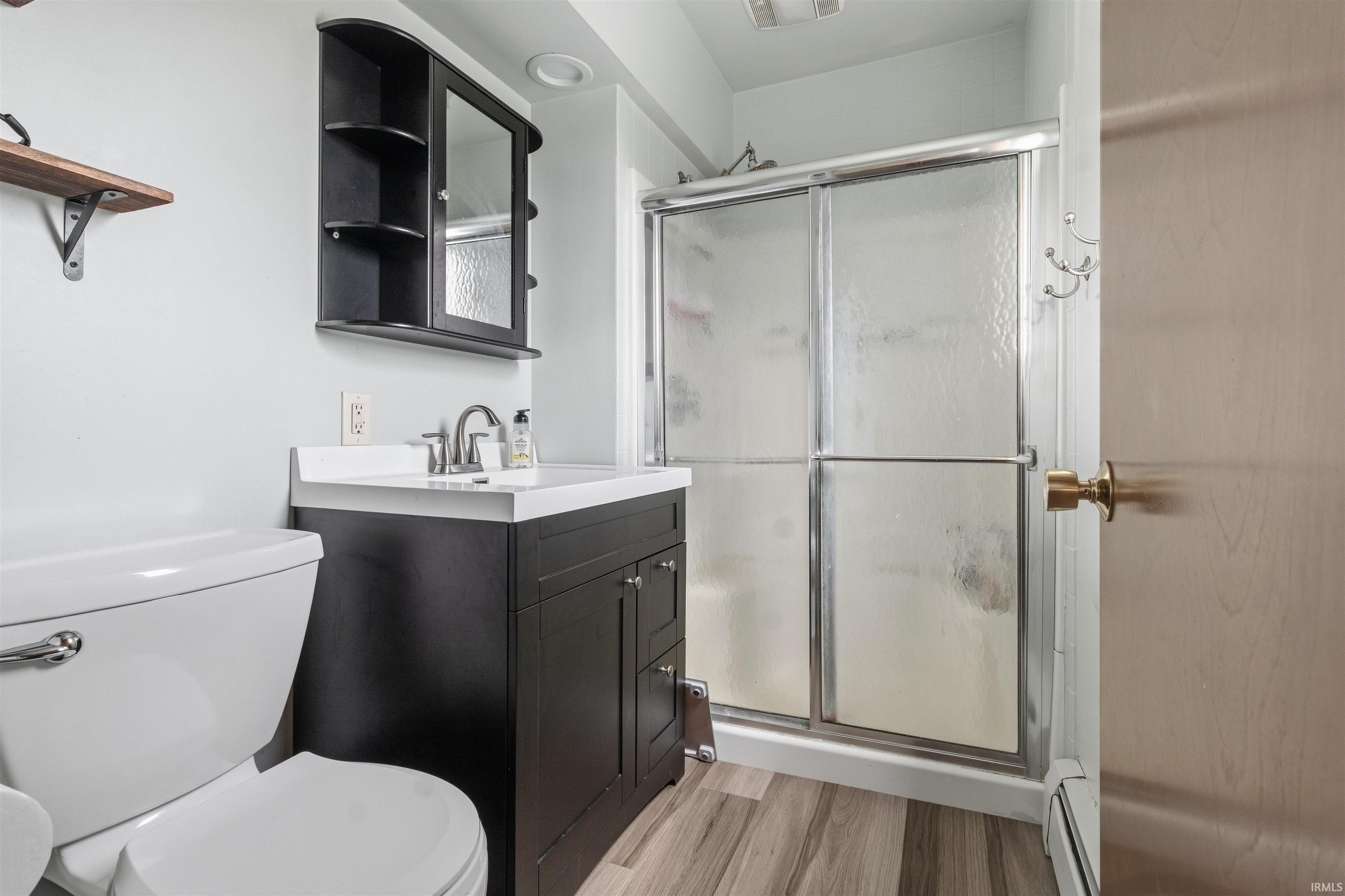 Full bathroom with a shower stall, vanity, baseboard heating, and light wood-style floors