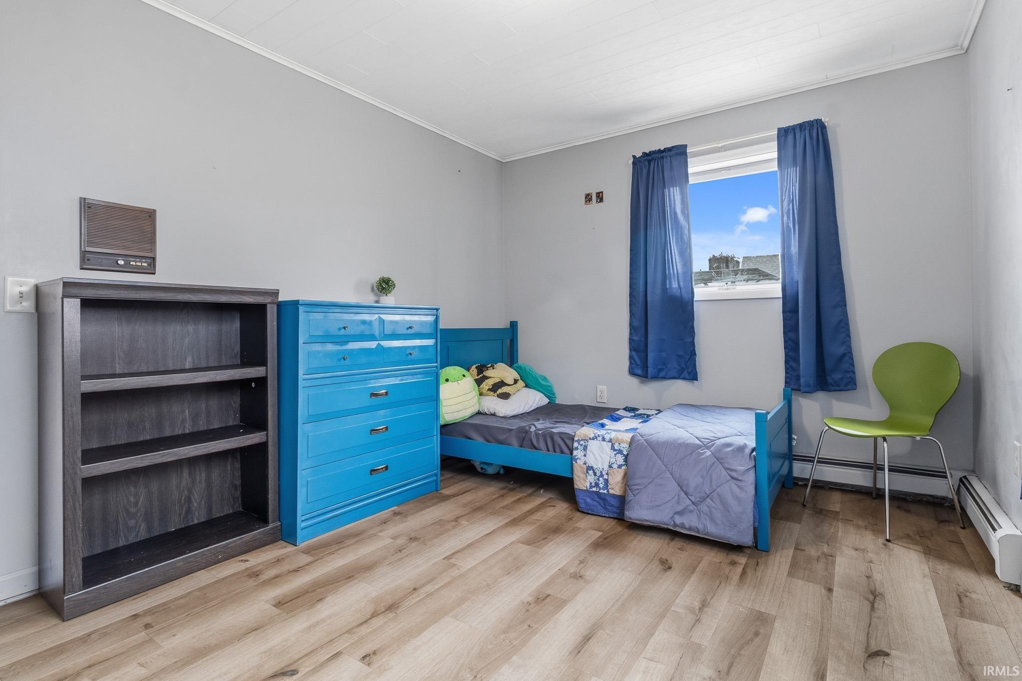 Bedroom with light wood-style flooring, crown molding, and a baseboard heating unit