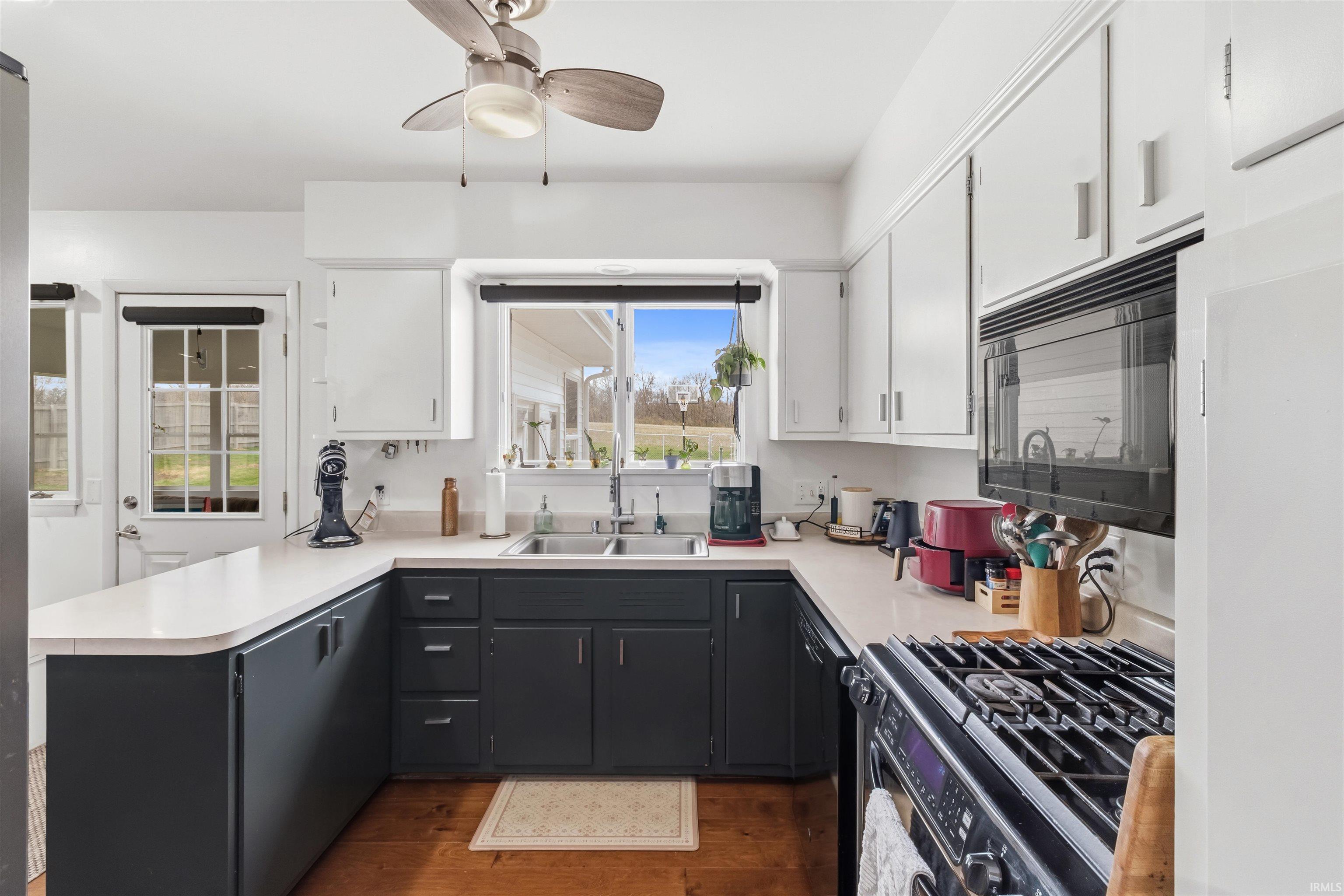 Two tone kitchen featuring dual tone cabinetry, black appliances, light countertops, dark wood-style floors, and ceiling fan