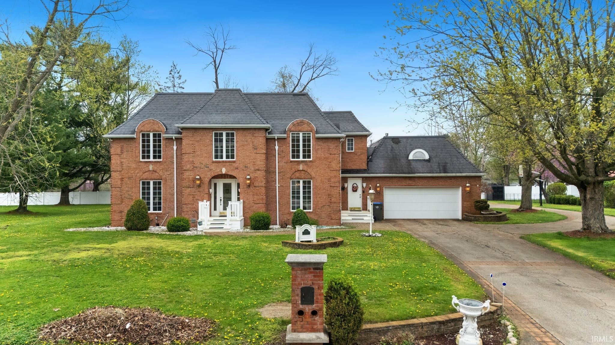 View of front of house with a front yard, an attached garage, driveway, roof with shingles, and brick siding
