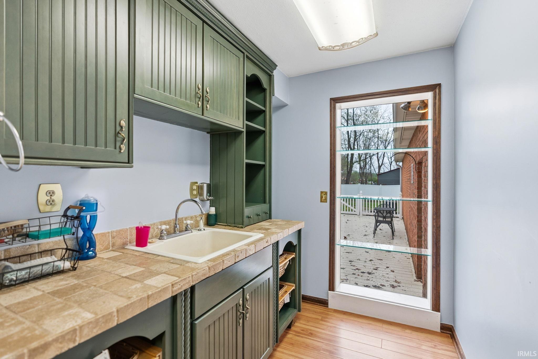 Kitchen featuring green cabinetry, open shelves, light countertops, and light wood-type flooring