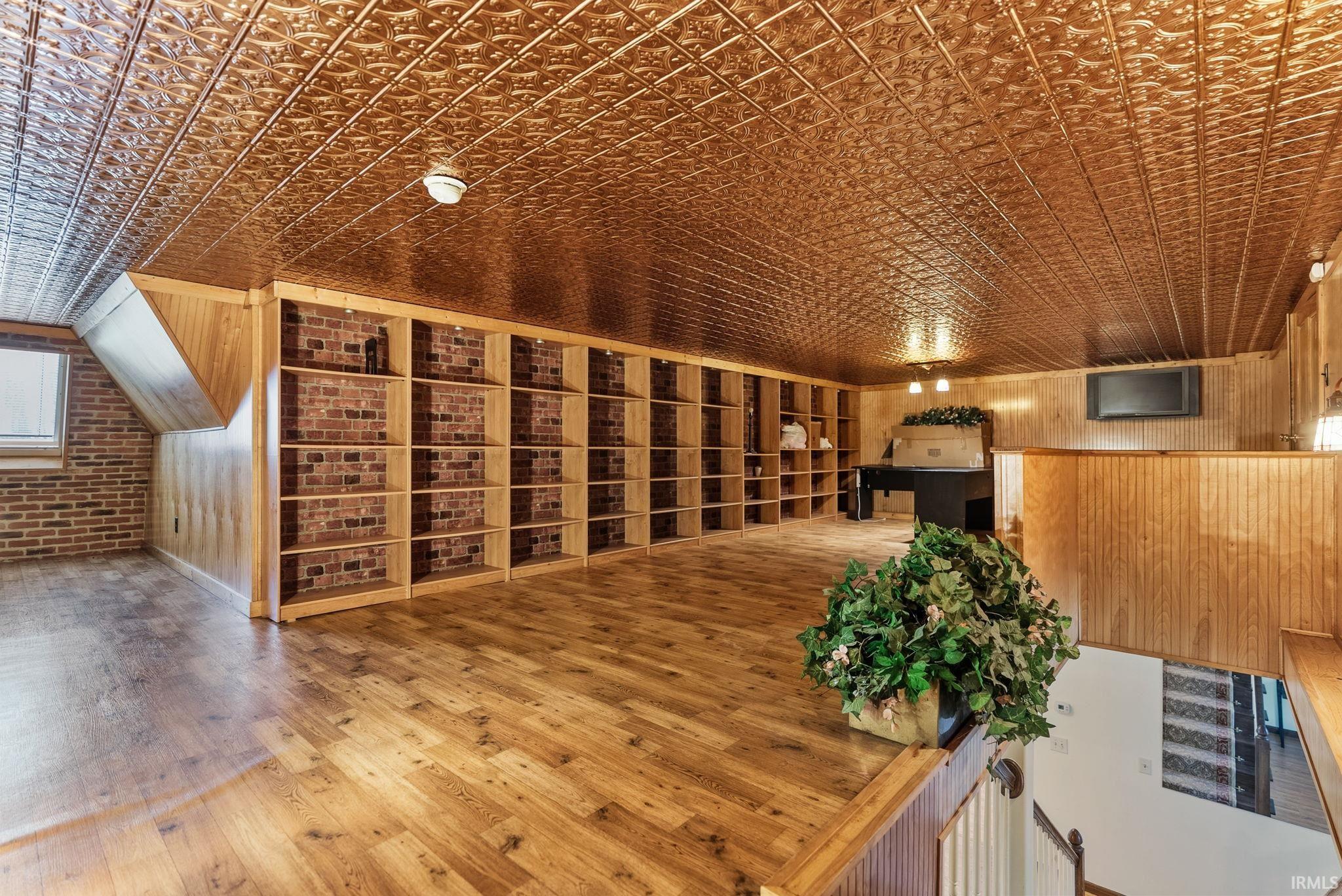 Bonus room with hardwood / wood-style floors, an ornate ceiling, wood walls, and brick wall