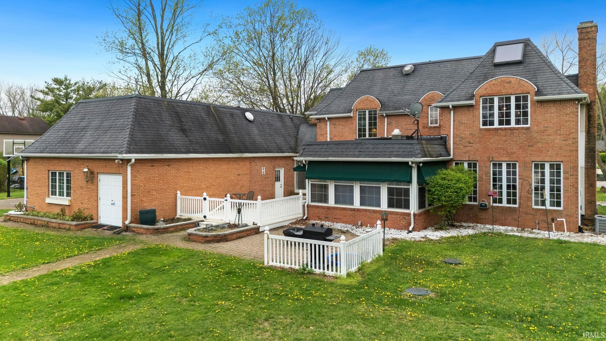 Back of house with a lawn, brick siding, a deck, and a shingled roof