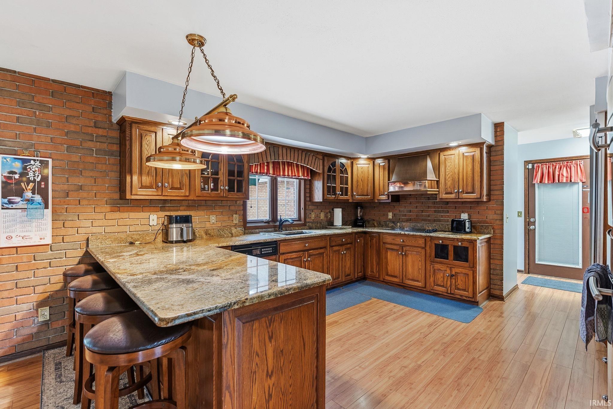 Kitchen featuring brick wall, a peninsula, light stone countertops, wood finish cabinetry, and light wood-type flooring