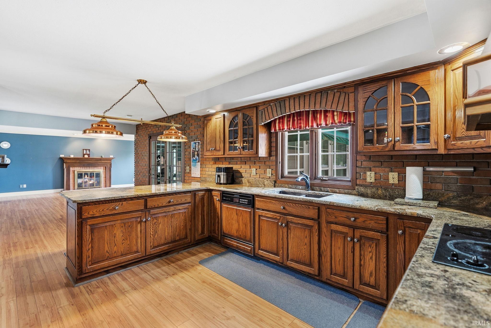 Kitchen featuring glass fronted cabinets, hanging light fixtures, black electric stovetop, dishwasher, and light wood finished floors