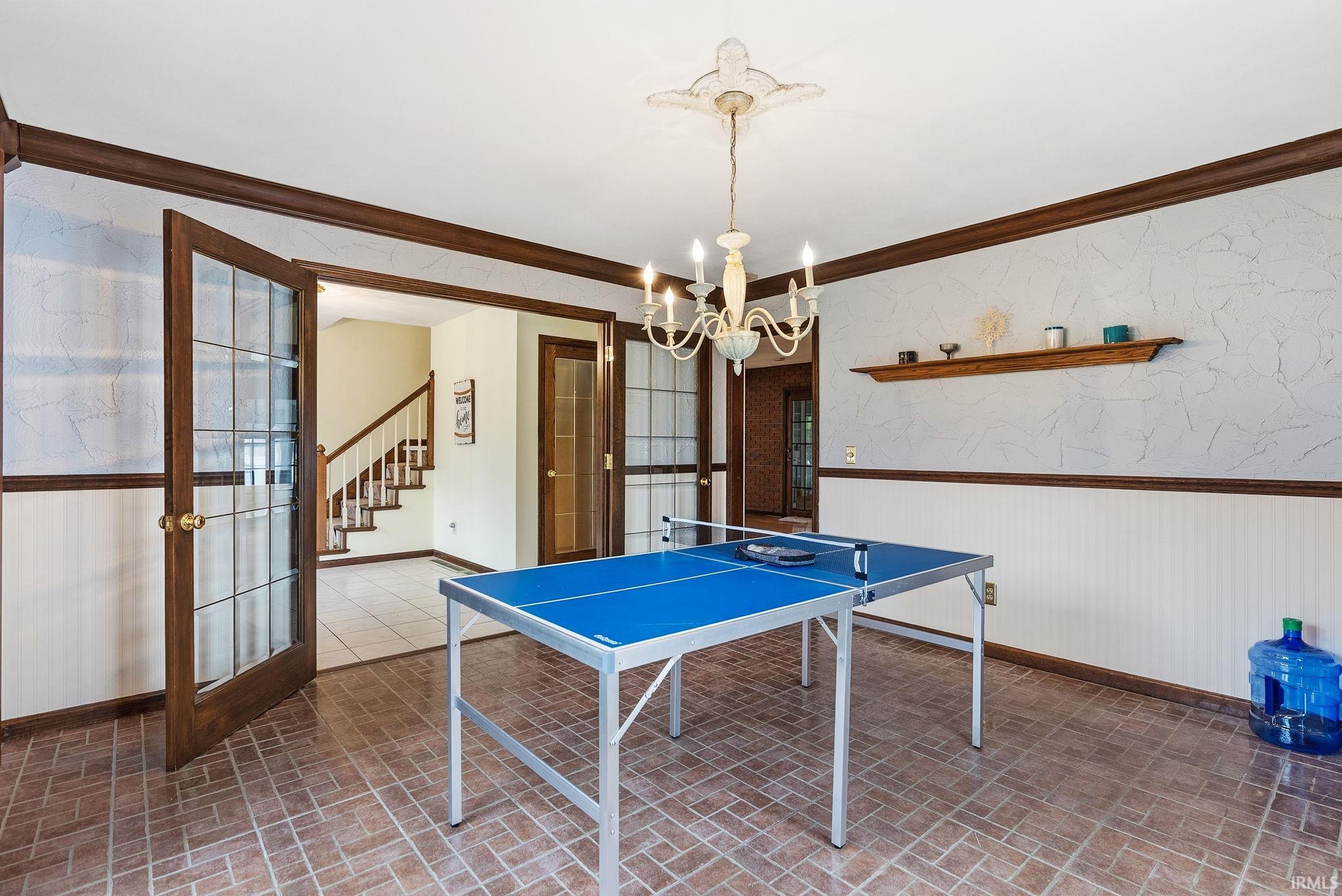 Rec room with wallpapered walls, a wainscoted wall, french doors, crown molding, and brick patterned floors
