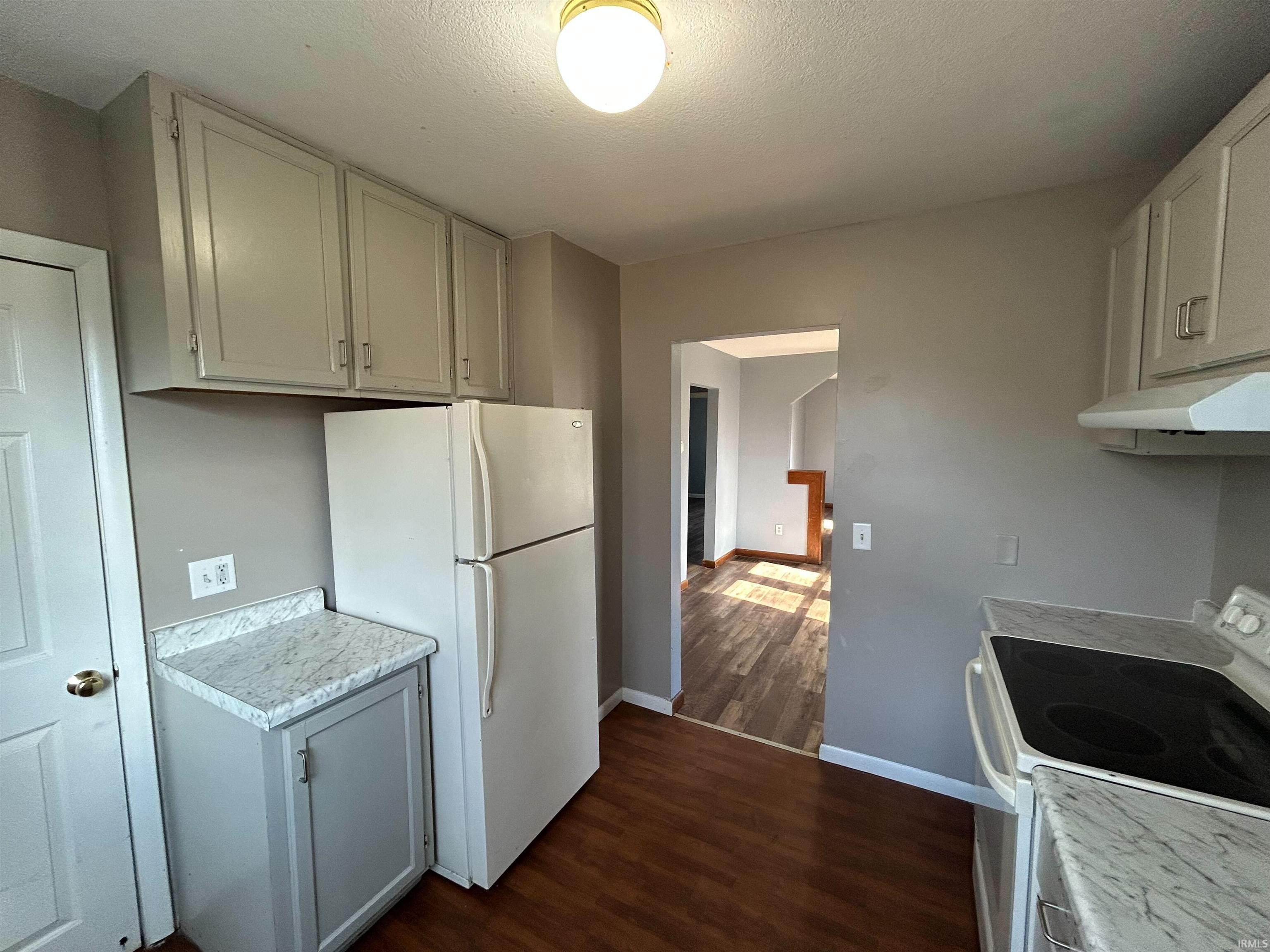 Kitchen with white appliances, light countertops, dark wood-style flooring, and a textured ceiling