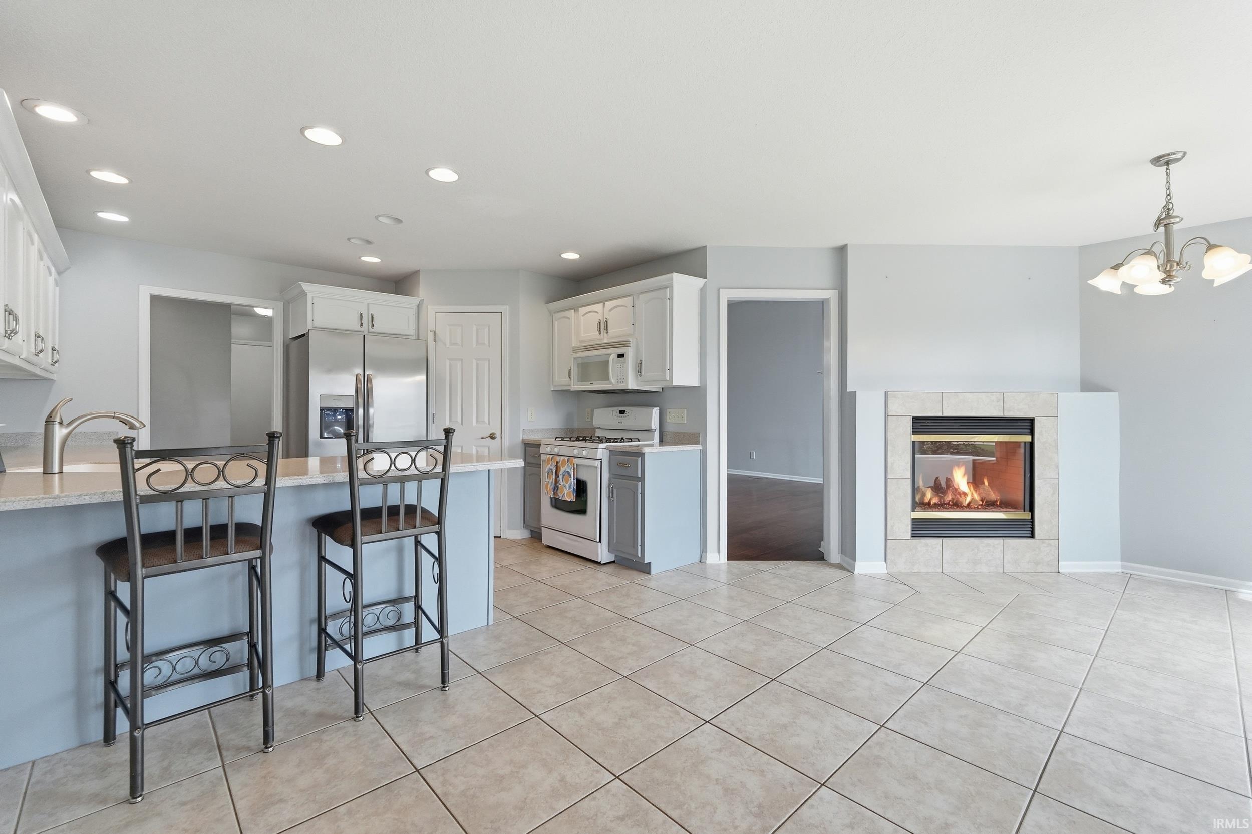 Kitchen with white appliances, a fireplace, a kitchen bar, white cabinets, and suspended lighting