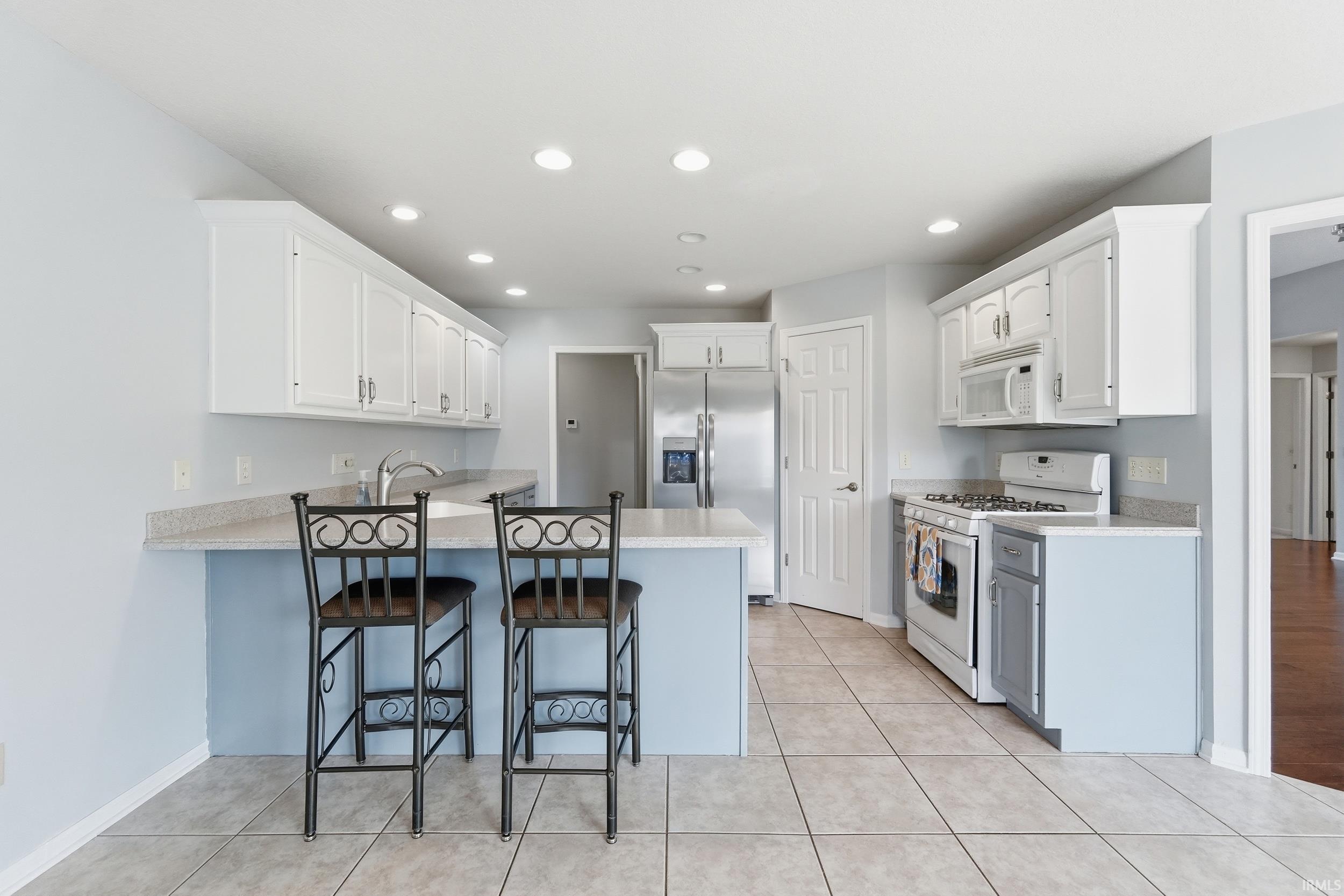 Kitchen featuring white appliances, white cabinetry, a breakfast bar, a peninsula, and light tile patterned floors