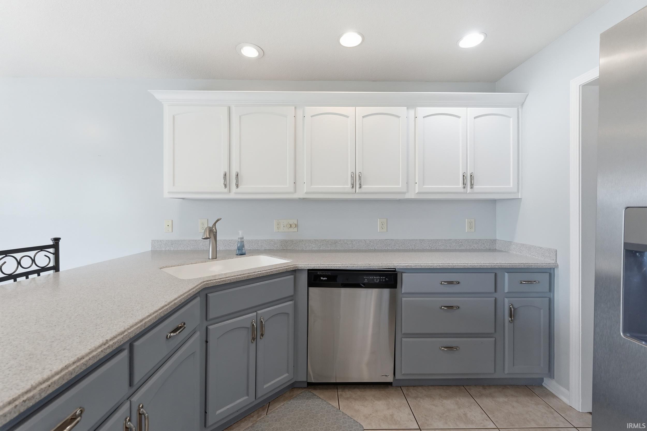 Kitchen featuring two tone color scheme, stainless steel appliances, light tile patterned flooring, light stone counters, and recessed lighting