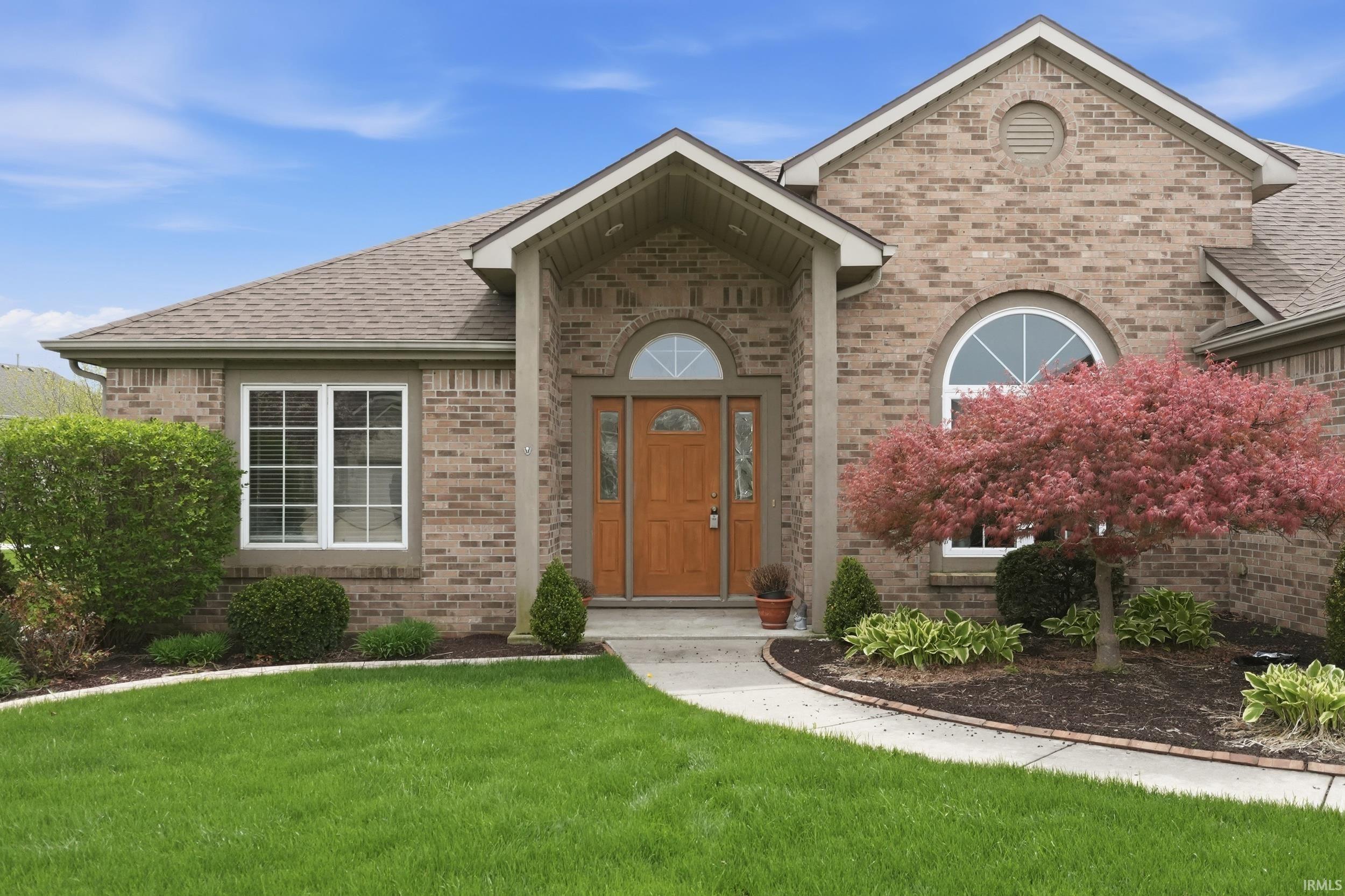 View of exterior entry featuring brick siding, a yard, and roof with shingles