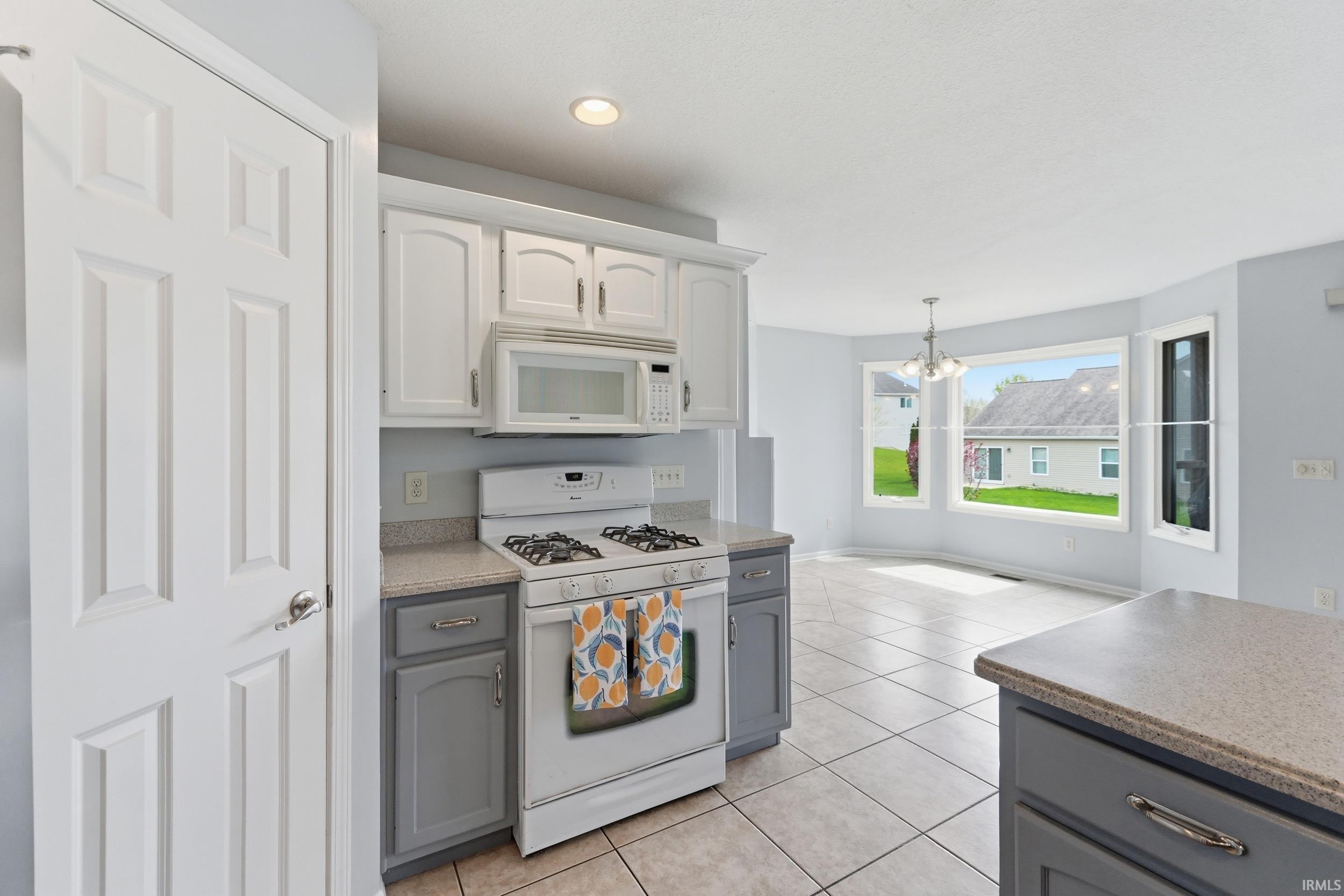 Two tone kitchen with white appliances, a chandelier, light tile patterned floors, and dual tone cabinetry