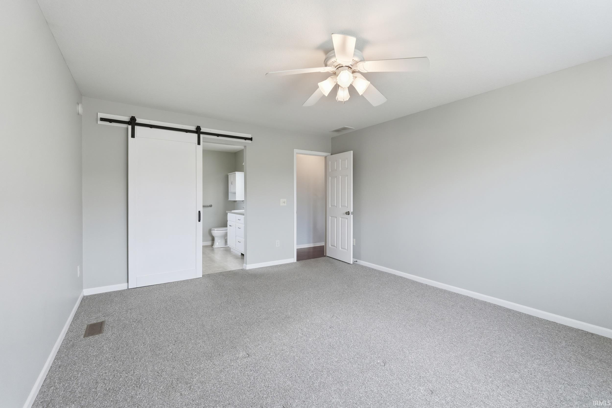 Unfurnished bedroom with a barn door, carpet floors, ensuite bath, and a ceiling fan