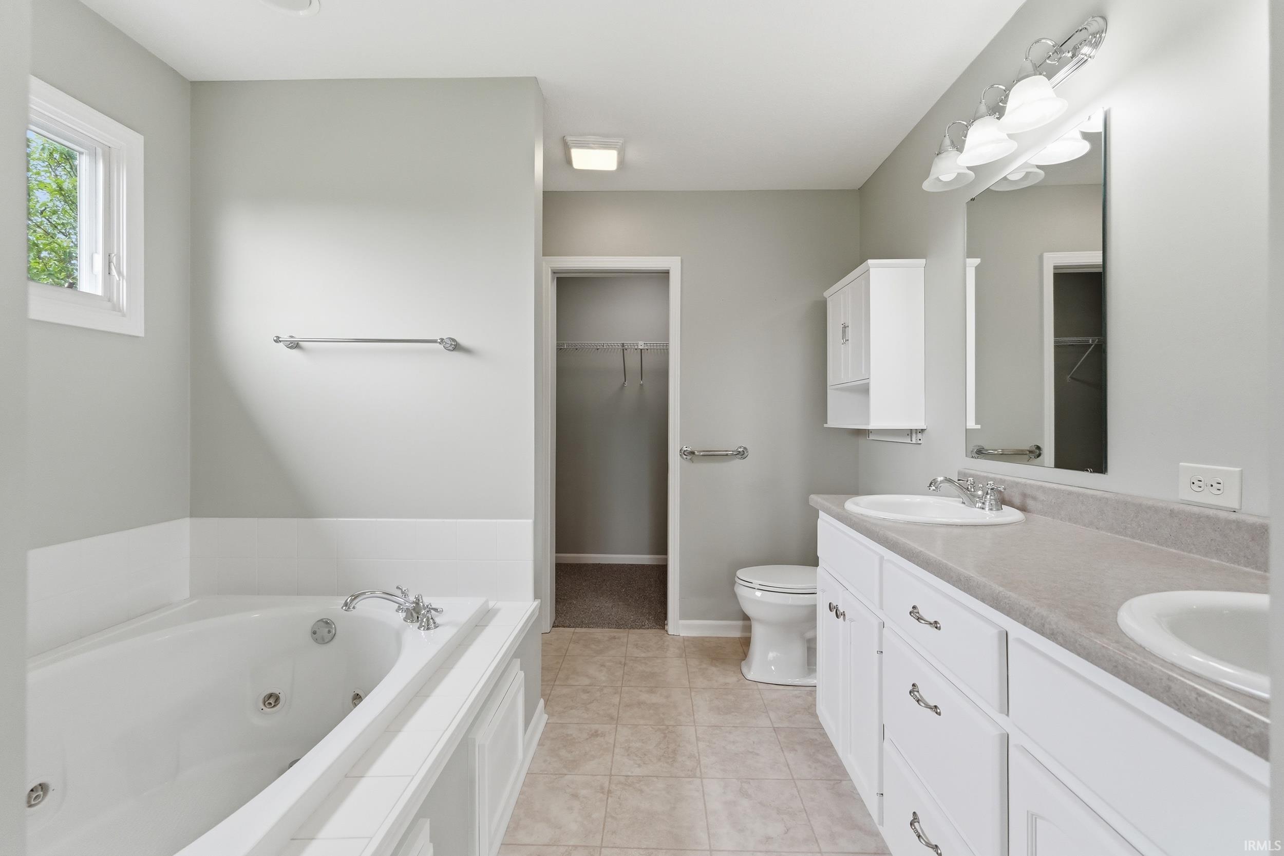 Full bathroom featuring double vanity, a whirlpool tub, a spacious closet, and light tile patterned flooring