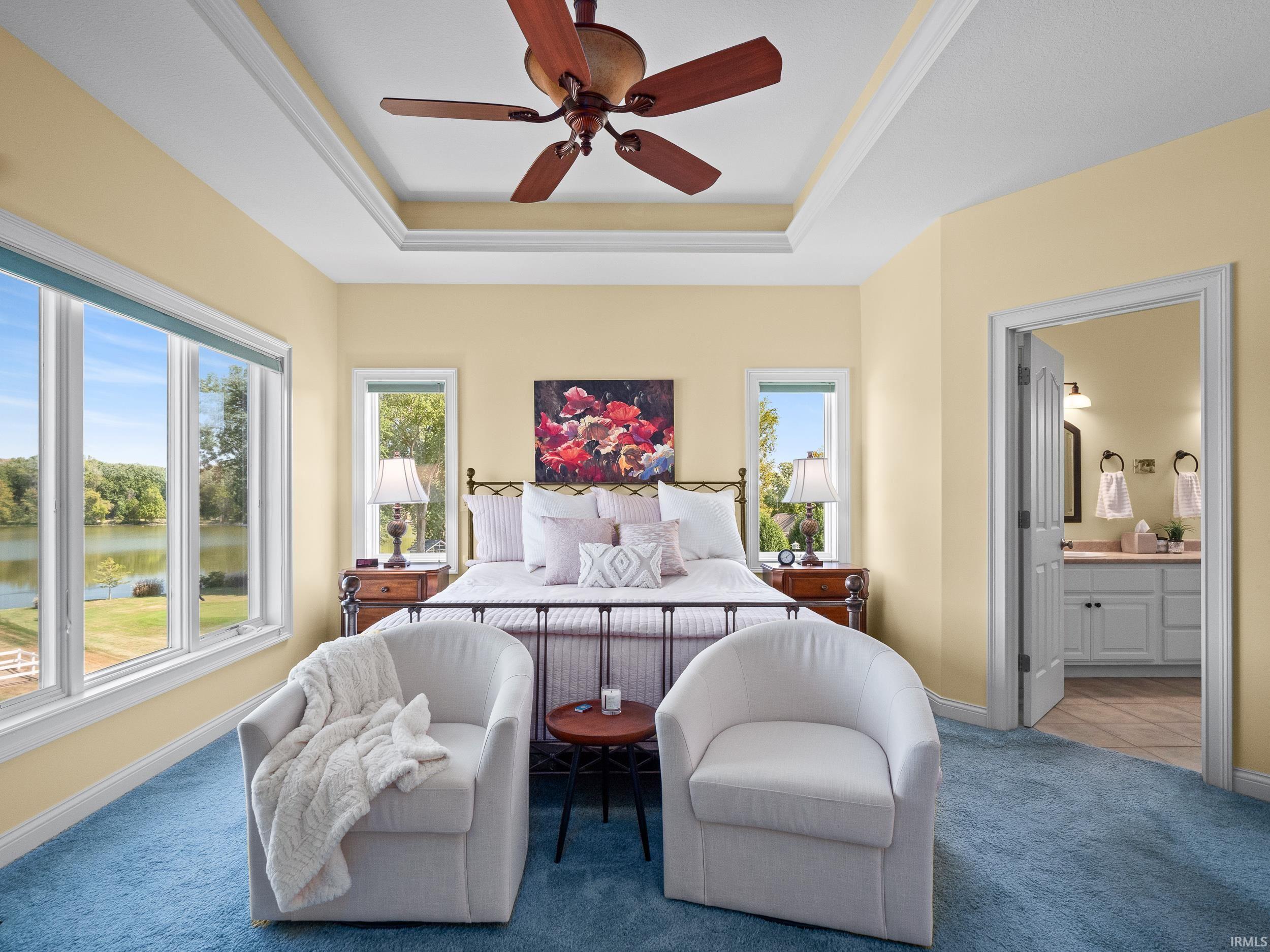 Bedroom with a water view, a ceiling fan, a raised ceiling, connected bathroom, and multiple windows