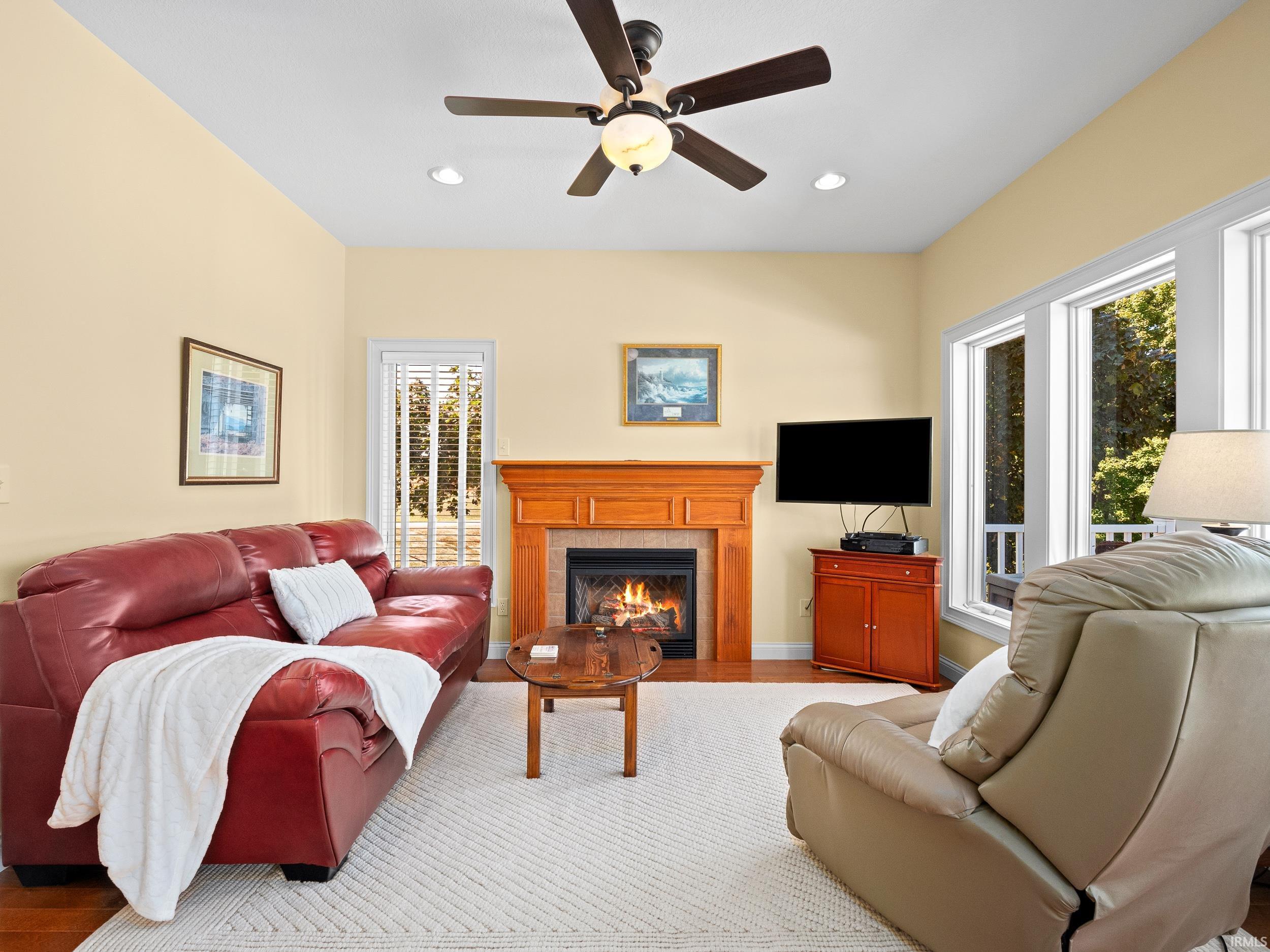 Living room featuring a tile fireplace, a ceiling fan, recessed lighting, and wood finished floors