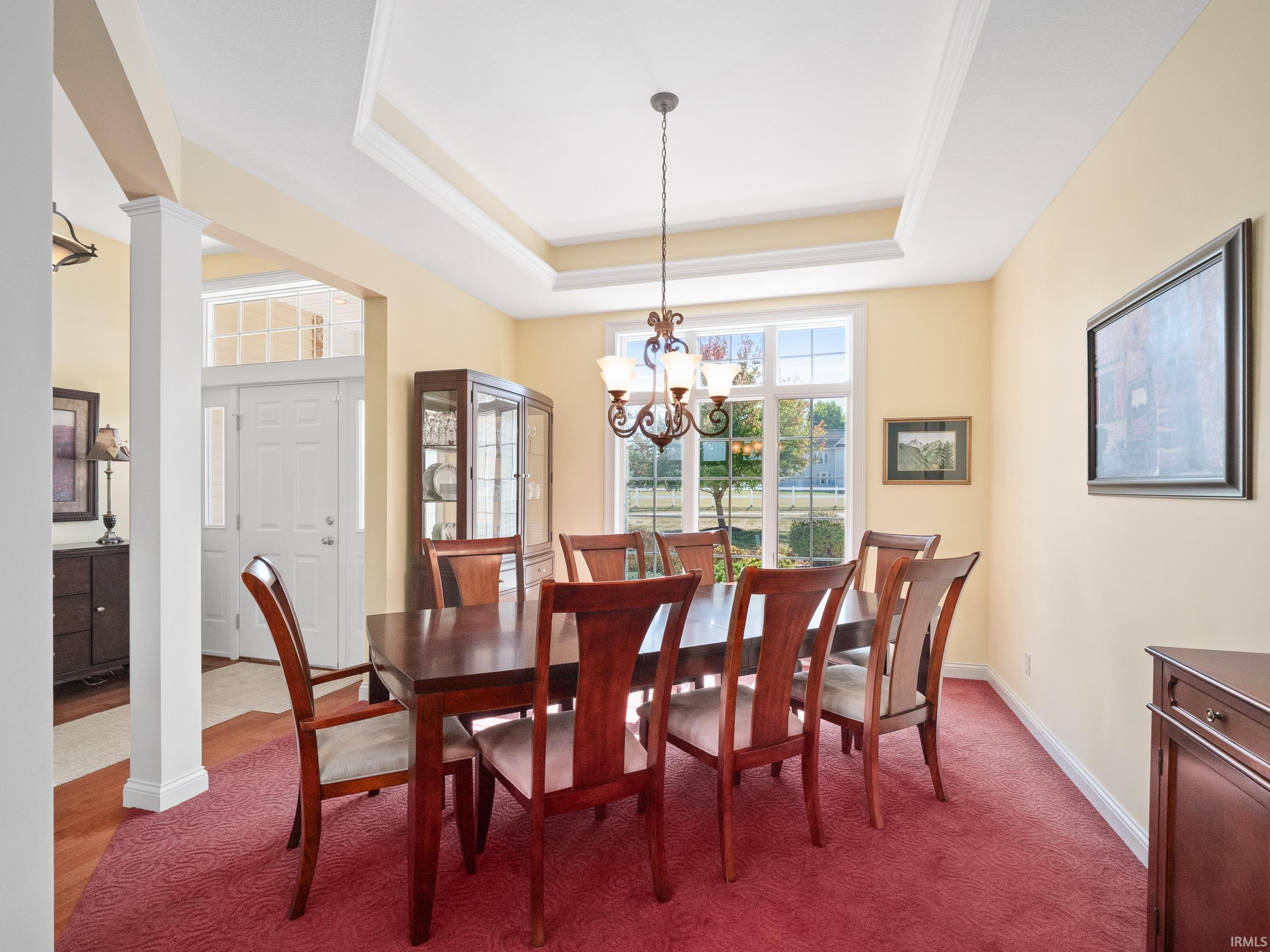 Dining room featuring a raised ceiling, a chandelier, and ornate columns
