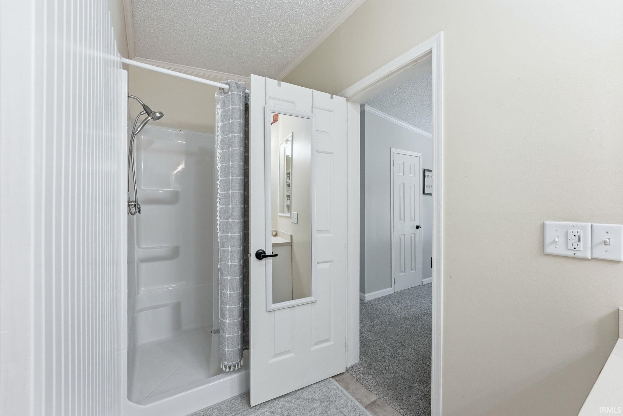 Bathroom with a textured ceiling, a shower stall, ornamental molding, and light carpet