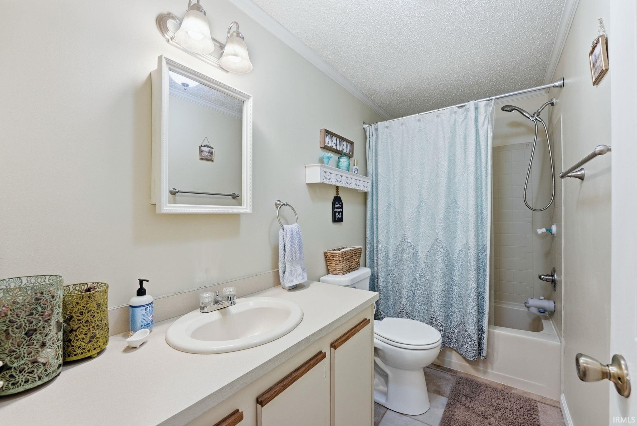 Bathroom with a textured ceiling, shower / bathtub combination with curtain, vanity, and crown molding