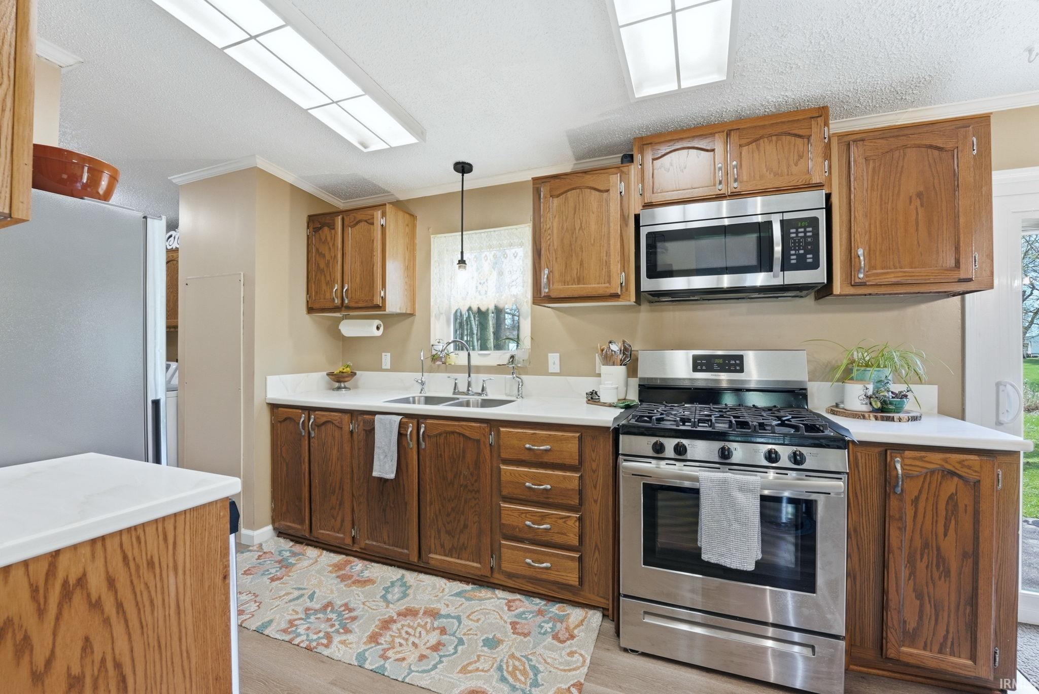 Kitchen featuring stainless steel appliances, ornamental molding, light countertops, wood finish cabinetry, and hanging light fixtures